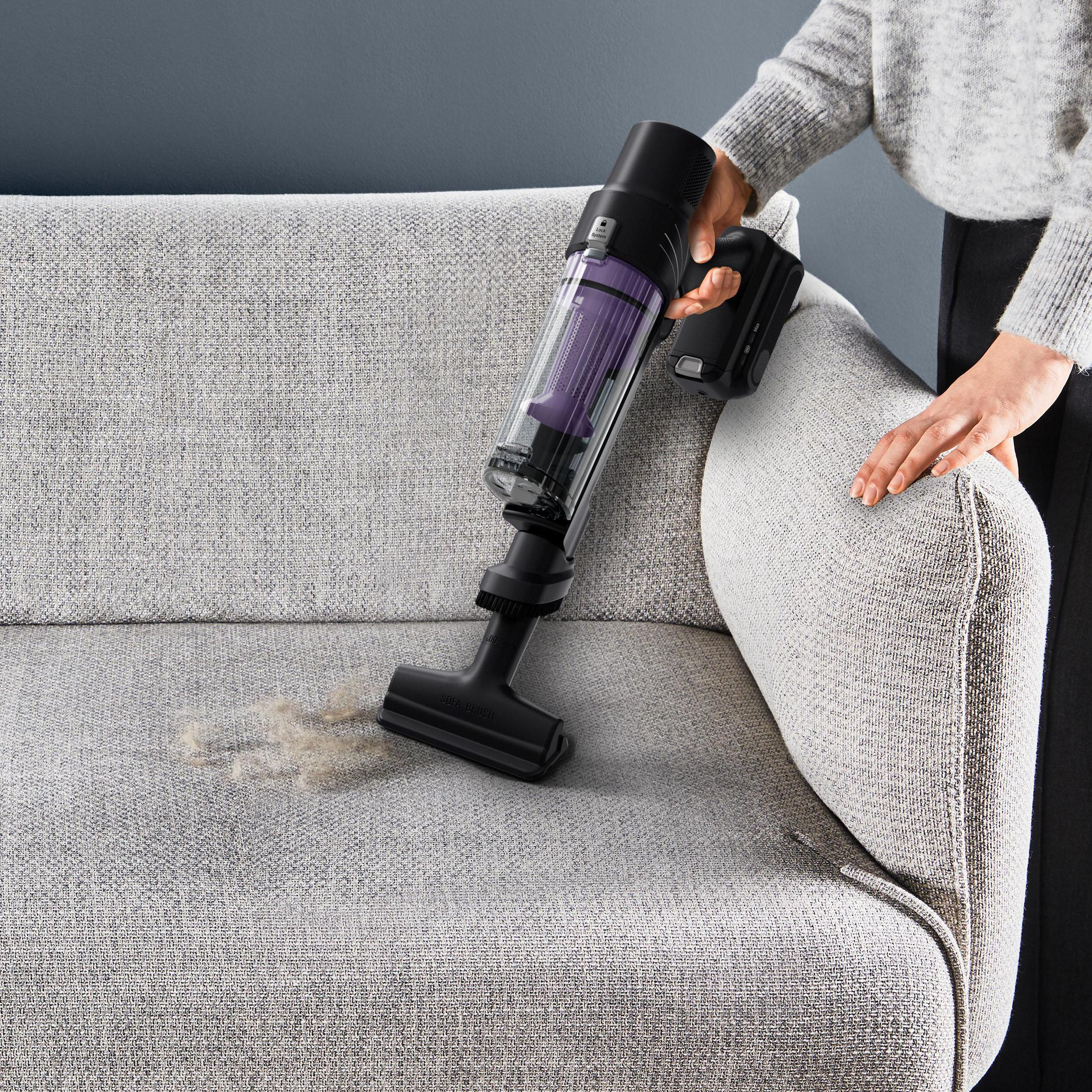 Eine Person, die ein Sofa absaugt, wobei Schmutz aus dem Stoff aufgesaugt wird.