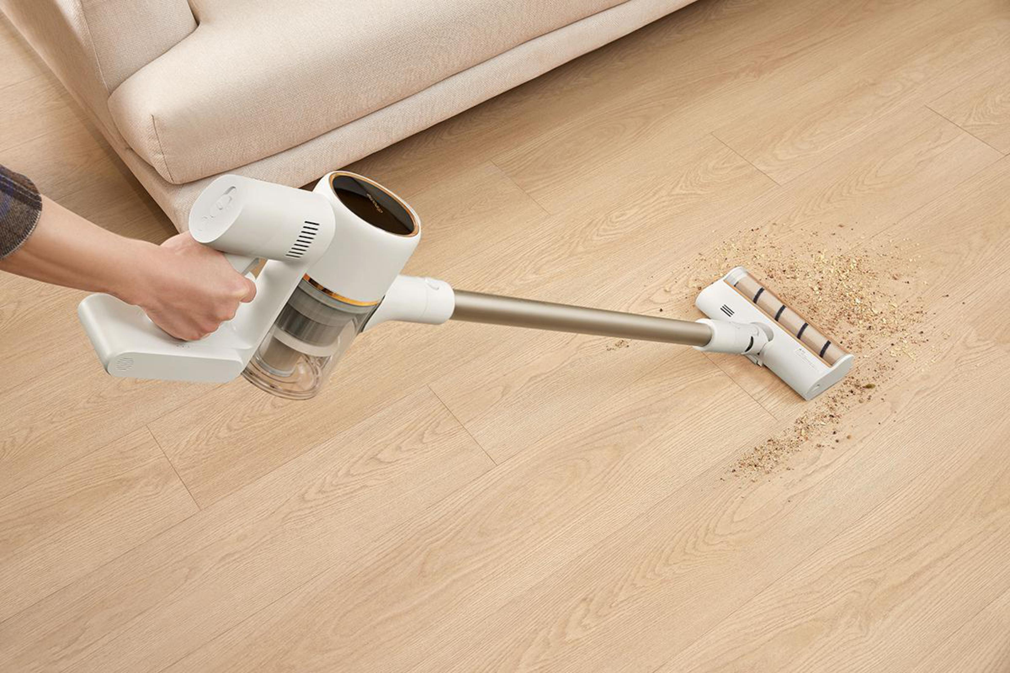 Mano sosteniendo una aspiradora blanca y dorada, limpiando un piso de madera.