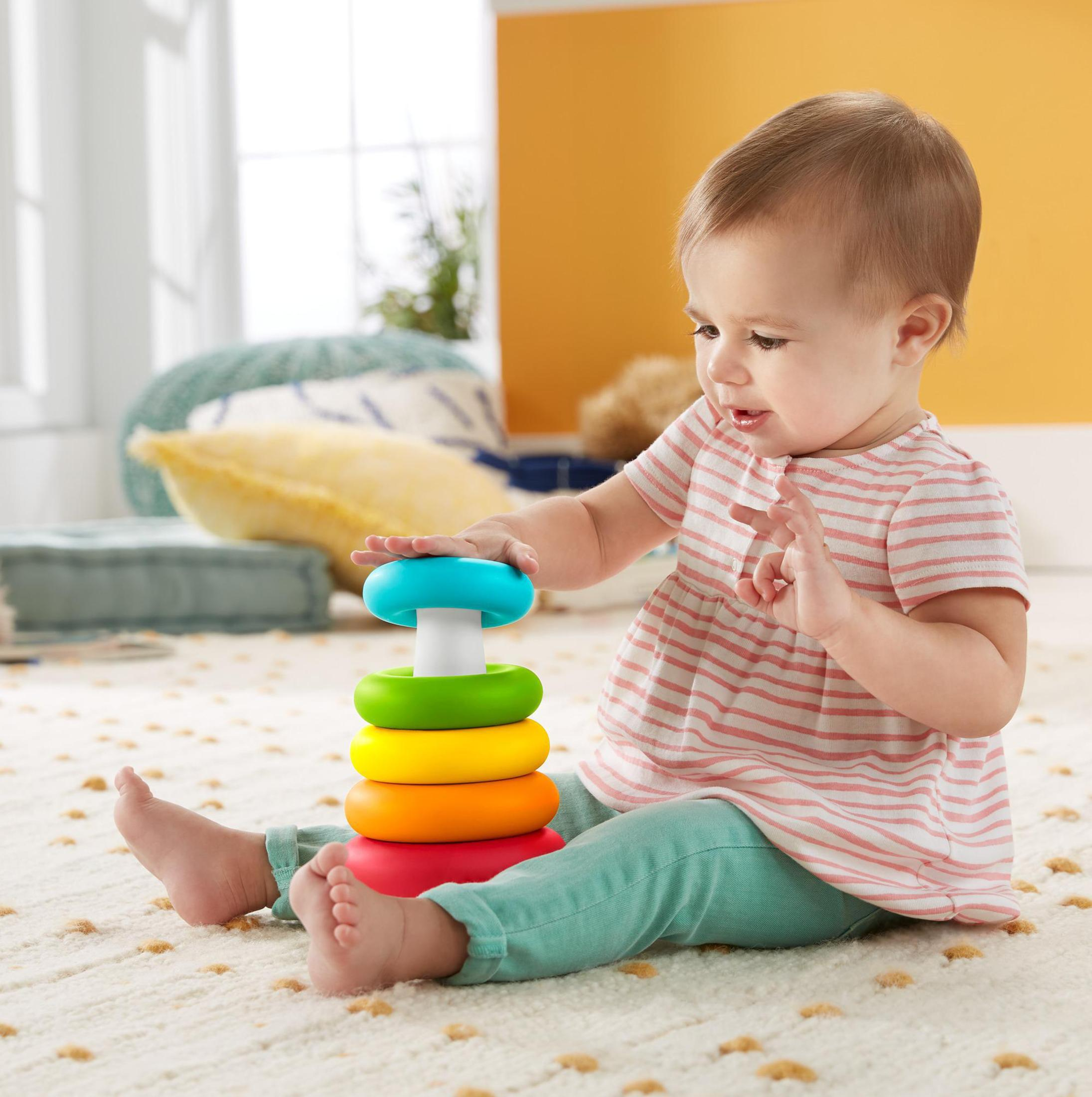 Ein Baby sitzt und spielt mit einem Stapelspielzeug. Das Spielzeug hat Ringe in Blau, Grün, Gelb, Orange und Rot.