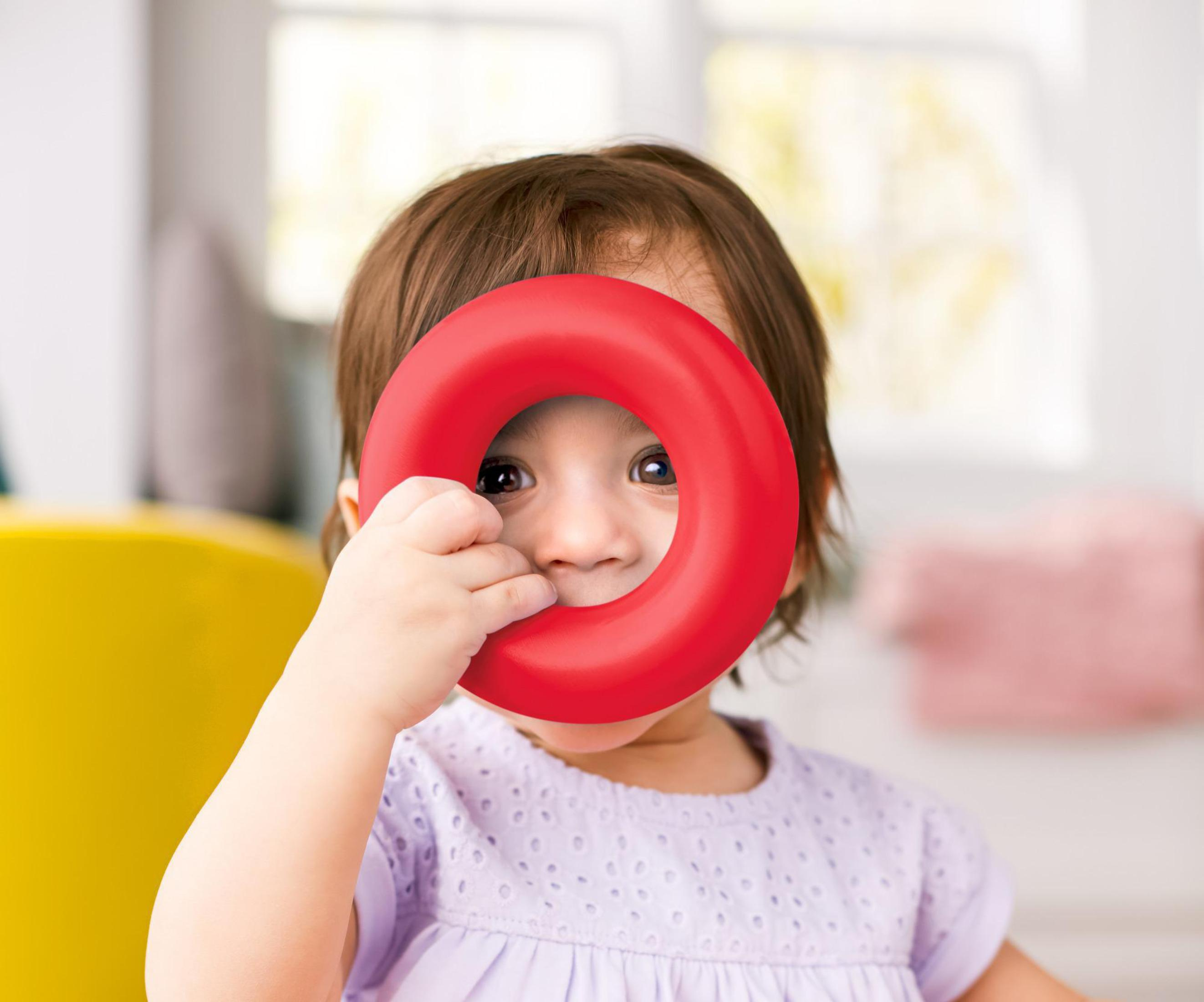 Ein Baby hält einen roten Ring vor seinem Gesicht. Das Baby schaut durch den Ring.