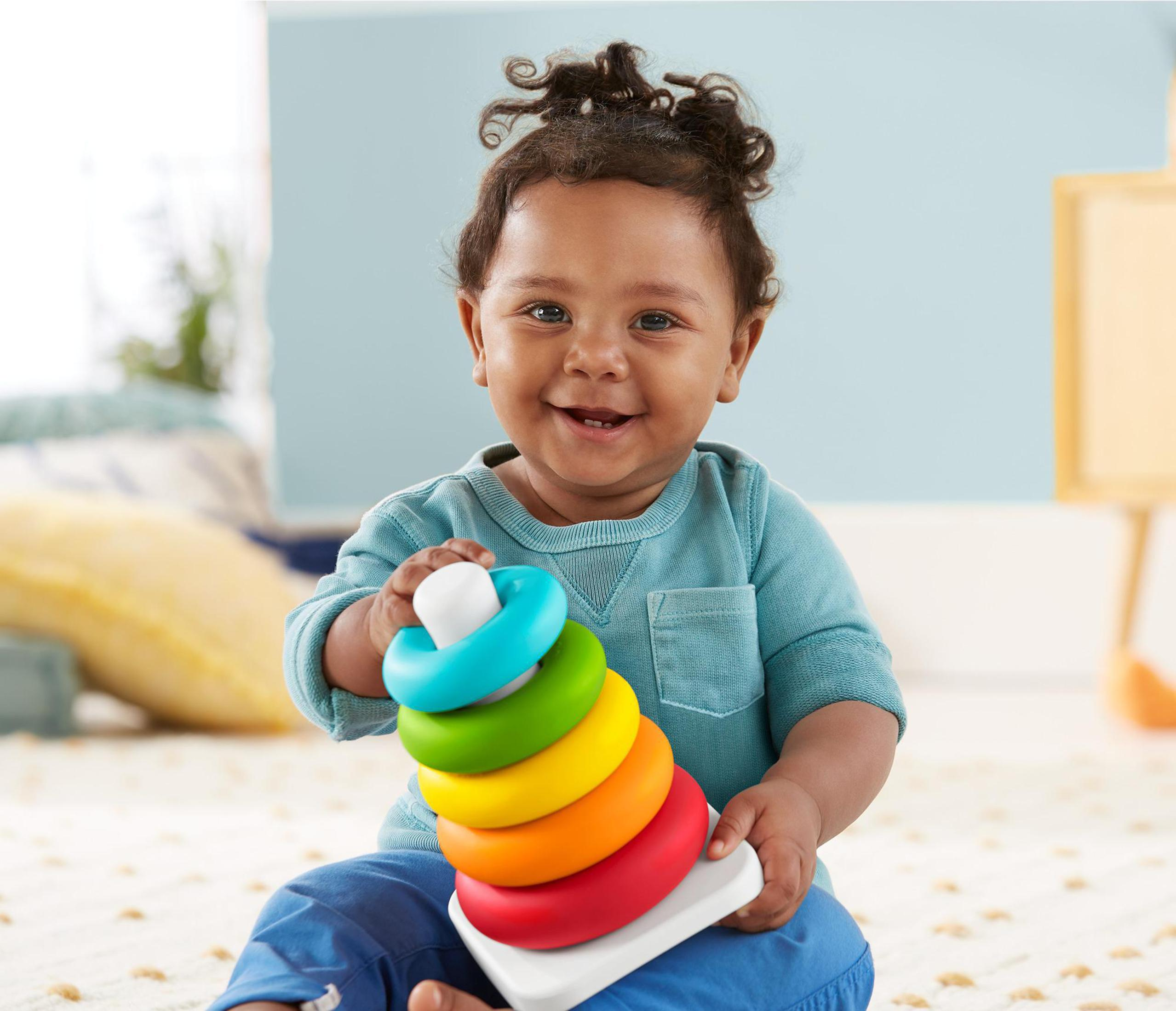 Ein Baby lächelt und hält das Stapelspielzeug mit blauen, grünen, gelben, orangenen und roten Ringen.