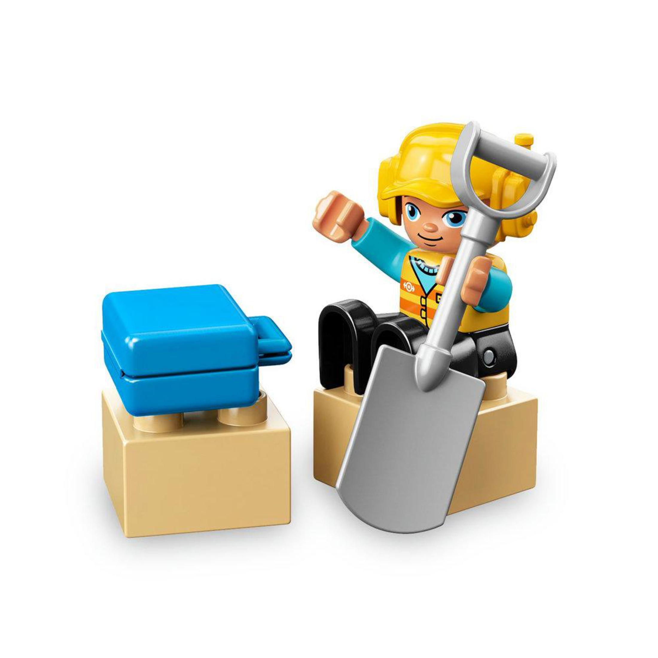 Figura LEGO Duplo che costruisce con blocco blu e pala. Lo sfondo è bianco.