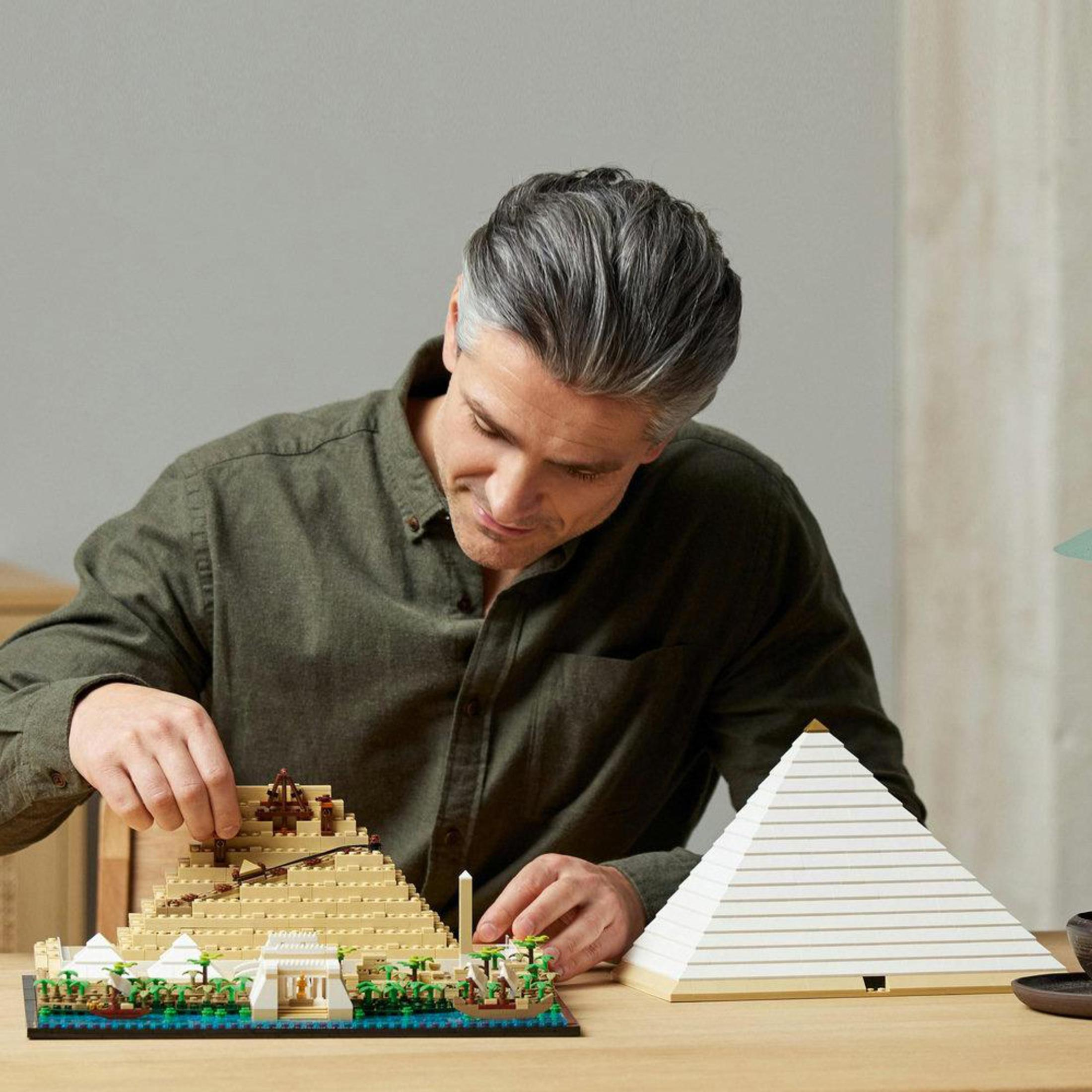 Ein Mann baut ein Lego-Pyramiden-Set. Das Set und eine fertige Pyramide stehen auf einem Tisch.