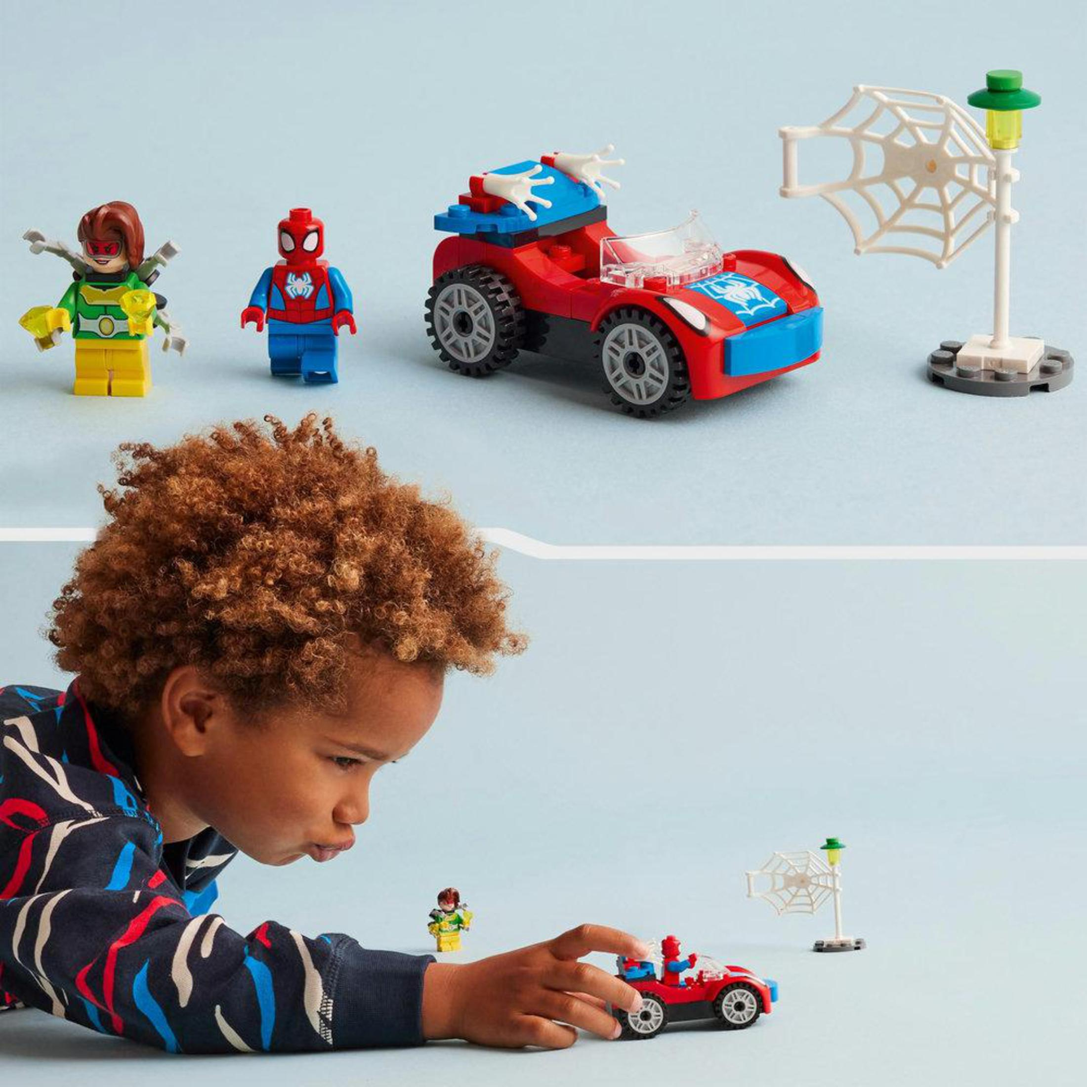 Lego-Set mit Spiderman, Auto und Laterne. Ein Kind spielt mit dem Set auf blauer Oberfläche.