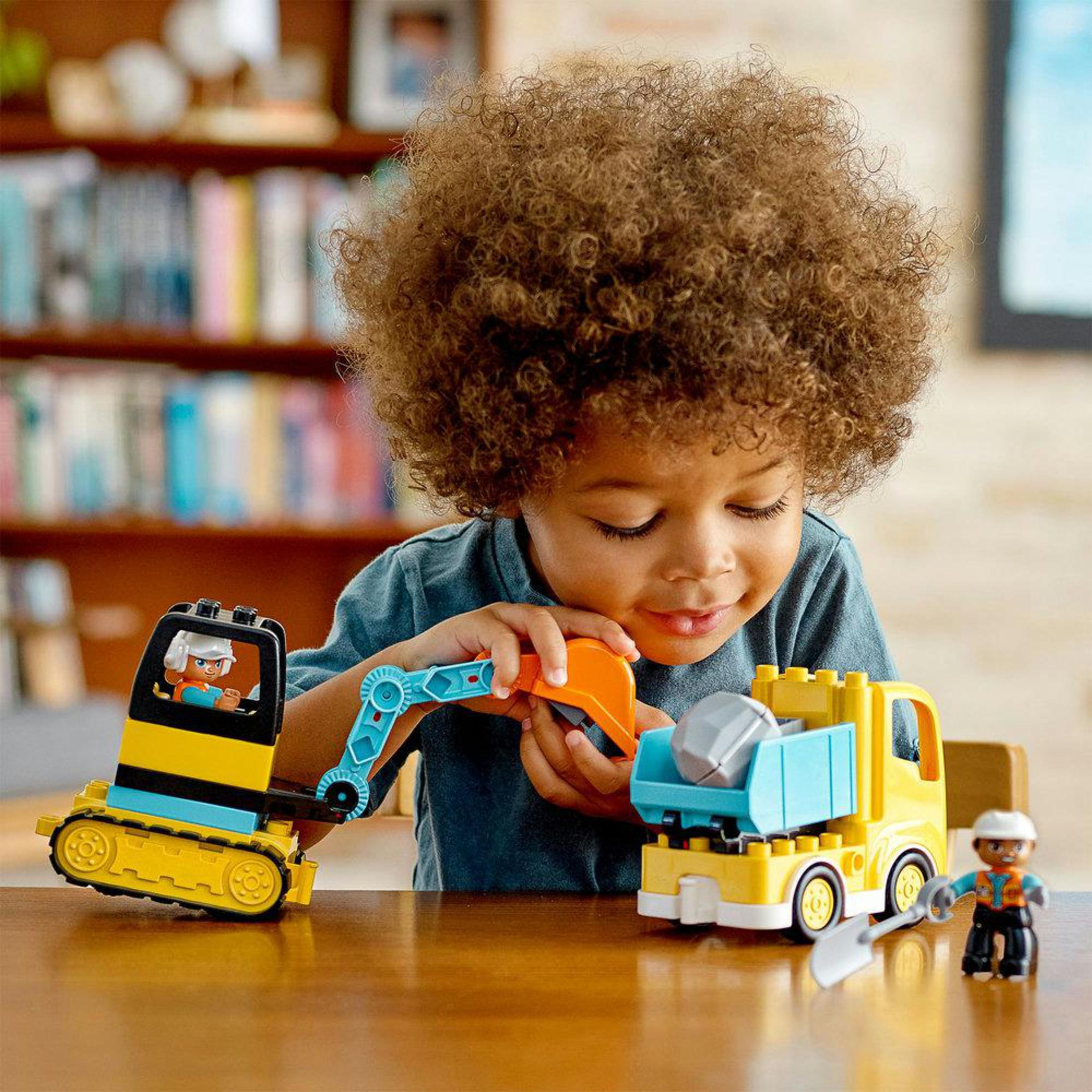 Een jong kind speelt met gele constructiespeelgoed, waaronder een vrachtwagen en graafmachine.