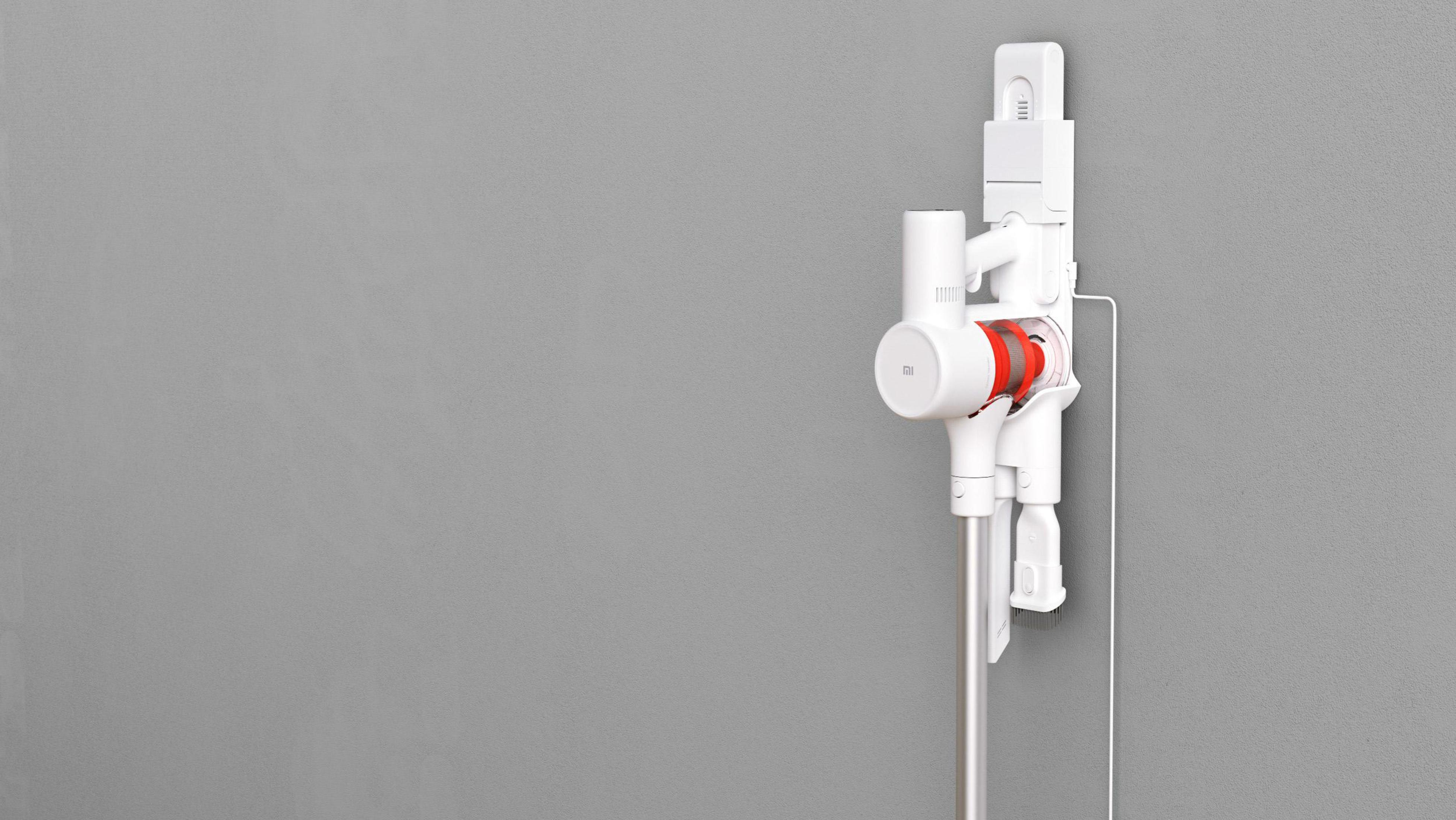 Biały odkurzacz bezprzewodowy na uchwycie ściennym na szarej ścianie, widok z boku.