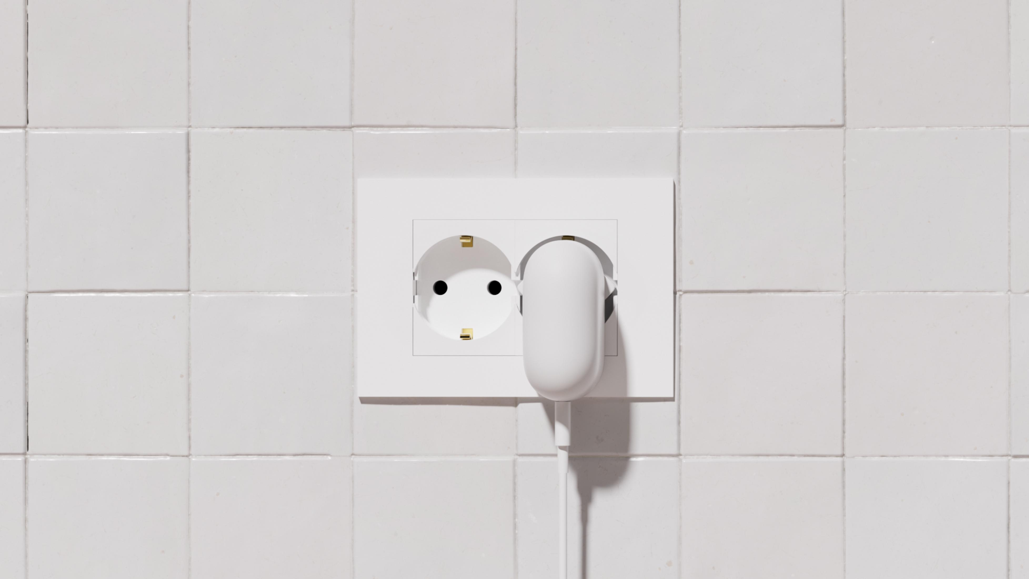 Presa elettrica bianca con spina bianca inserita. Sfondo piastrellato bianco.