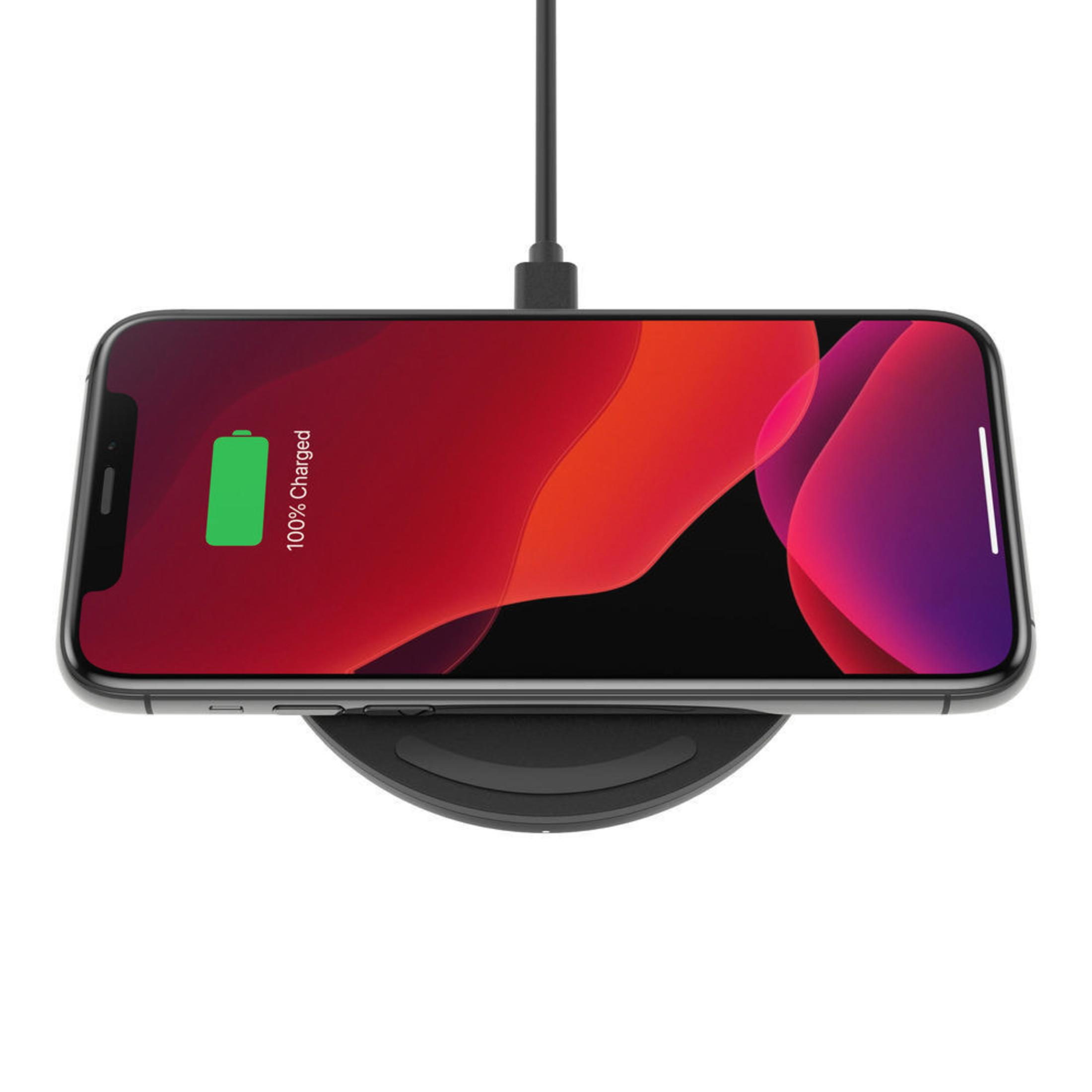 Schwarzes Telefon, das auf einem schwarzen kabellosen Ladegerät geladen wird. Bildschirm zeigt 100%.