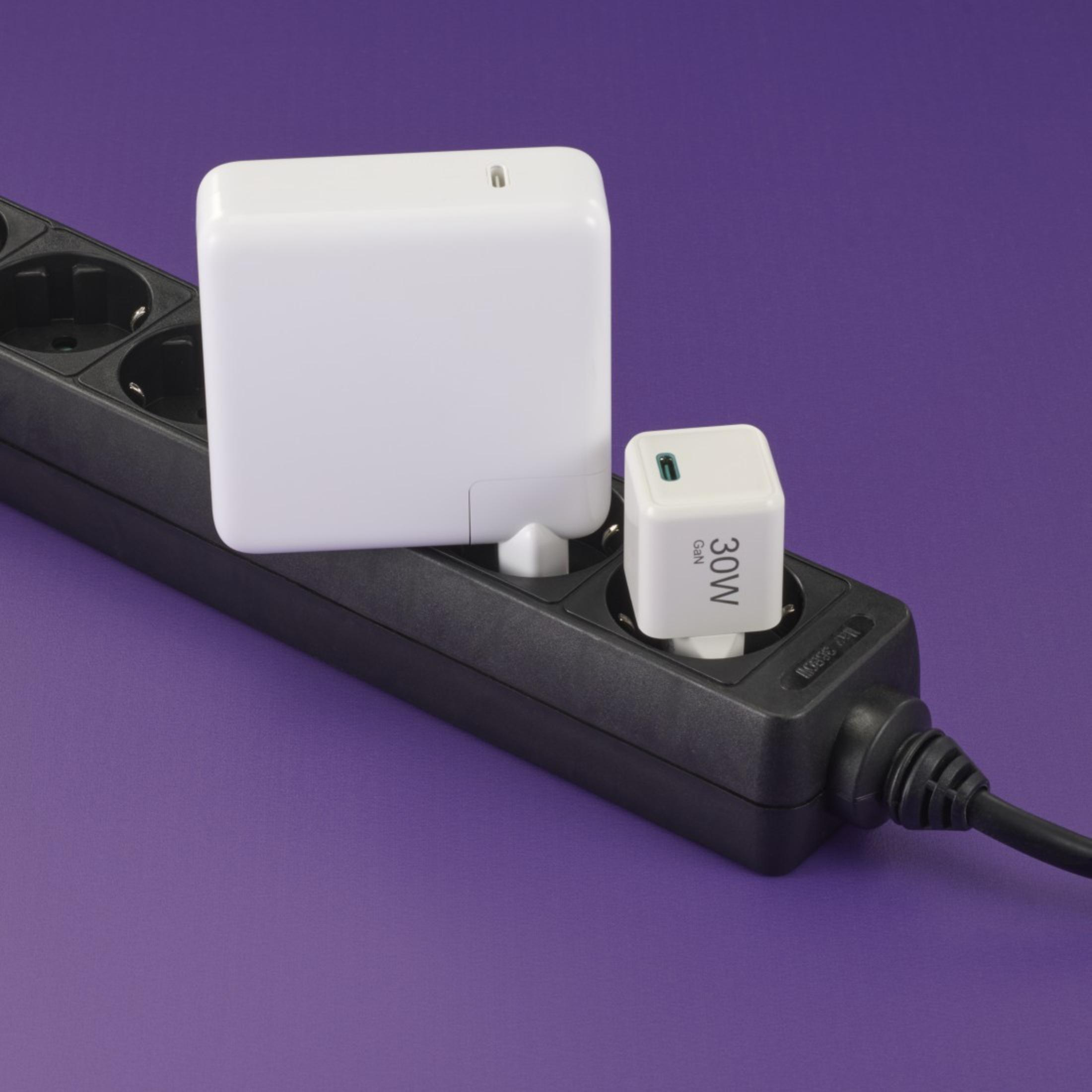 Adaptadores de corriente blancos enchufados a una regleta negra. Fondo morado.