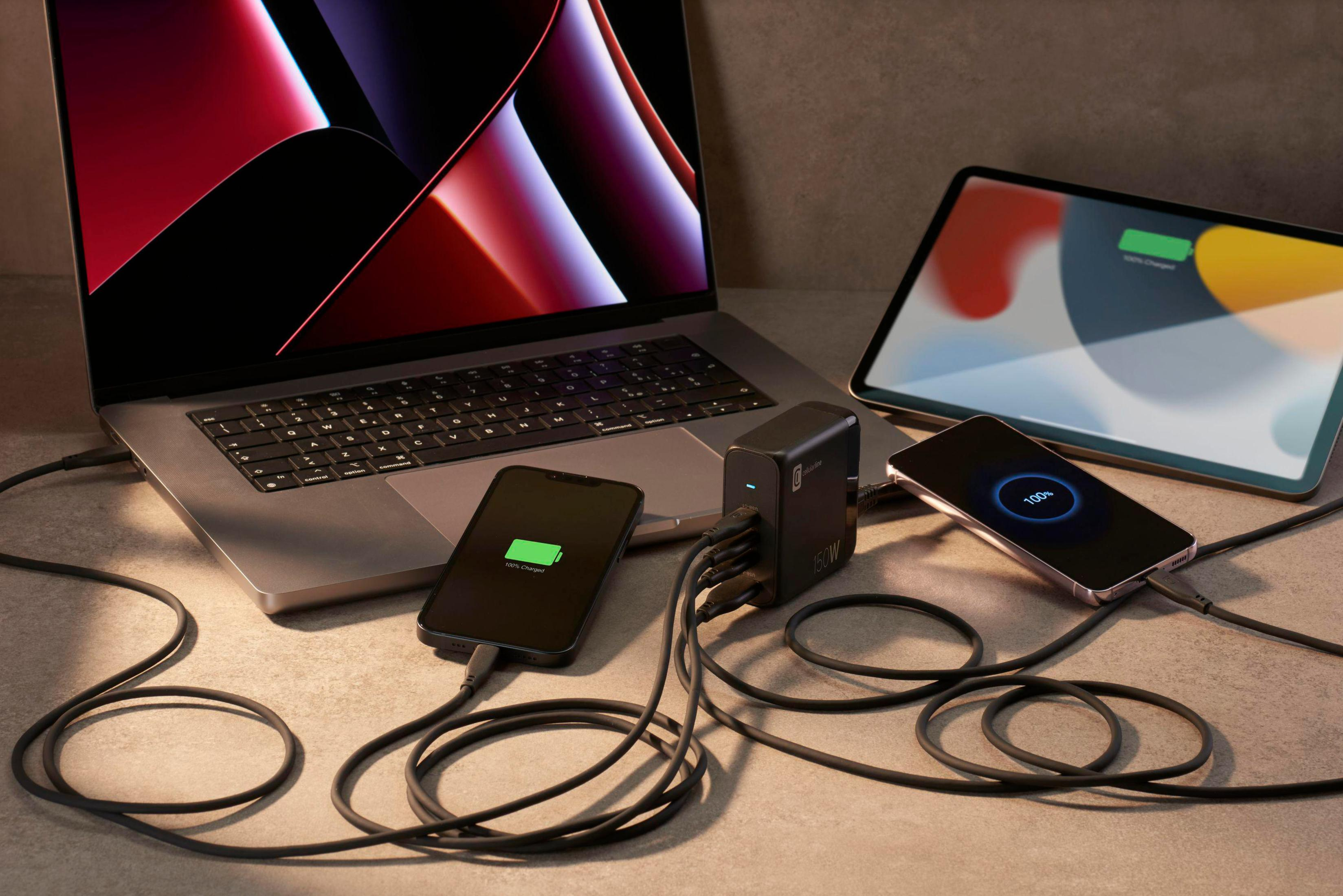 Mehrere Geräte laden von einem schwarzen Ladegerät. Laptop, Tablet und Telefone. Kabel verbunden.