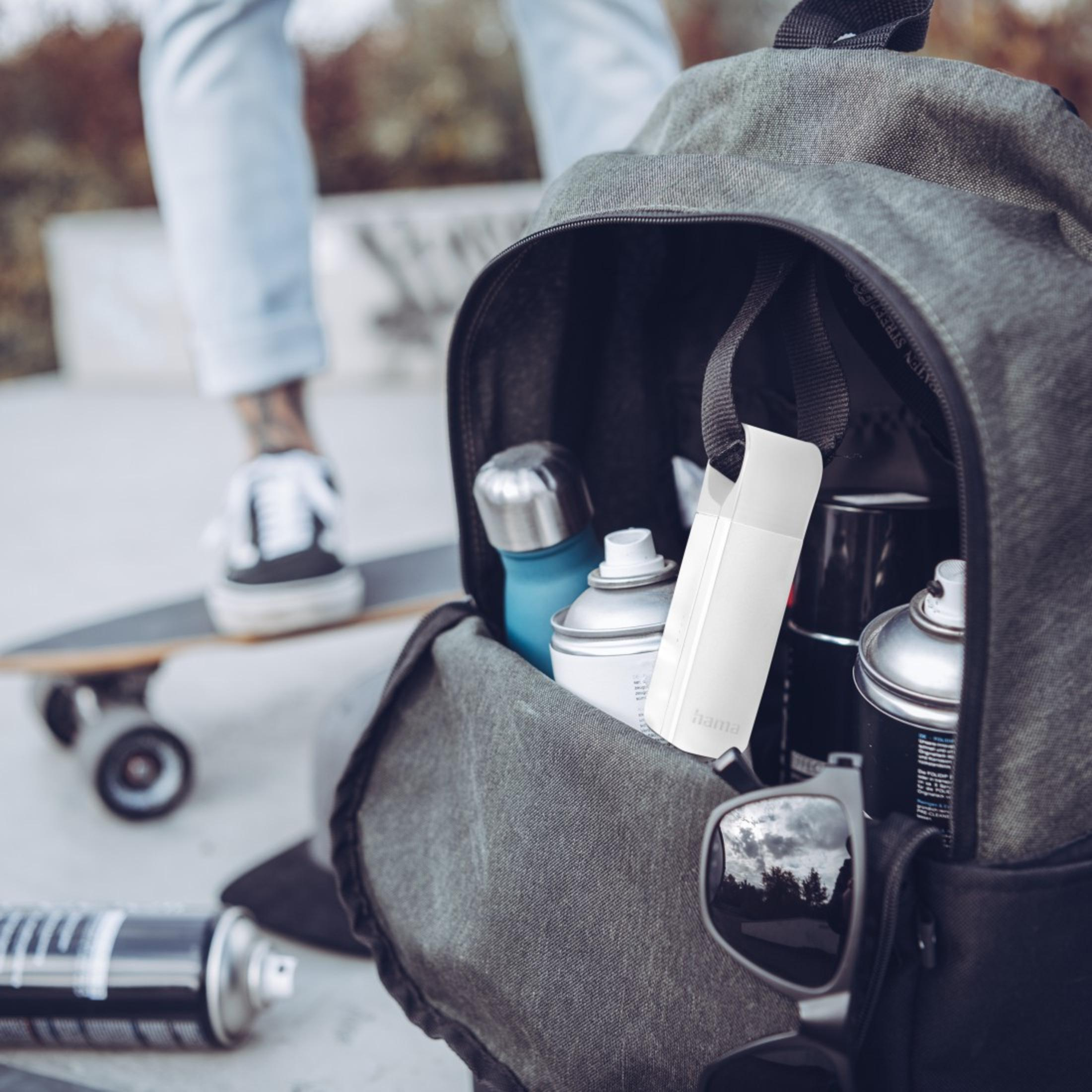 Zaino con bombolette spray all'interno. Gambe di una persona e skateboard sullo sfondo. Occhiali da sole sopra.