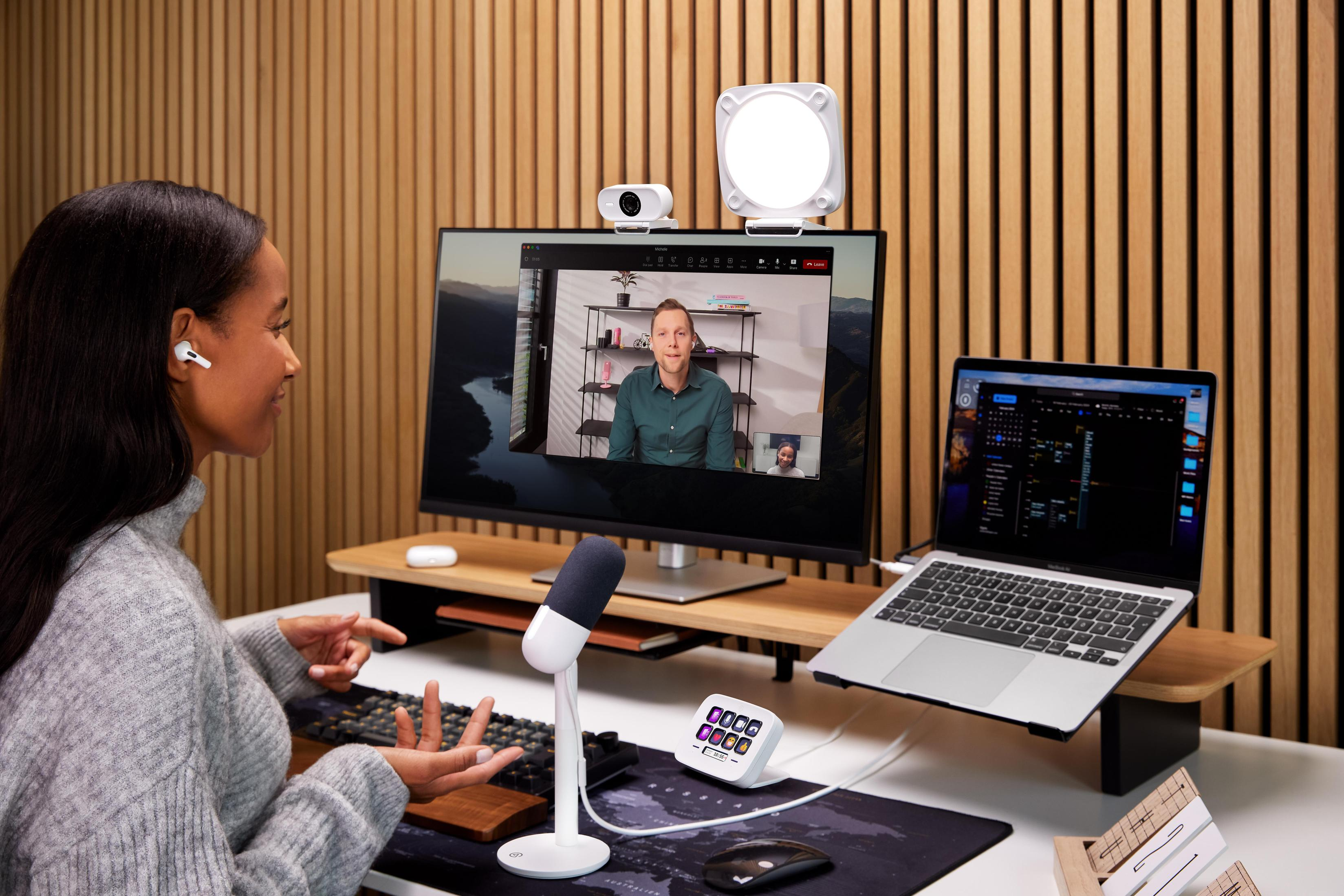 Frau in einem Videoanruf-Setup. Ein Monitor, ein Laptop und ein Mikrofon sind sichtbar.