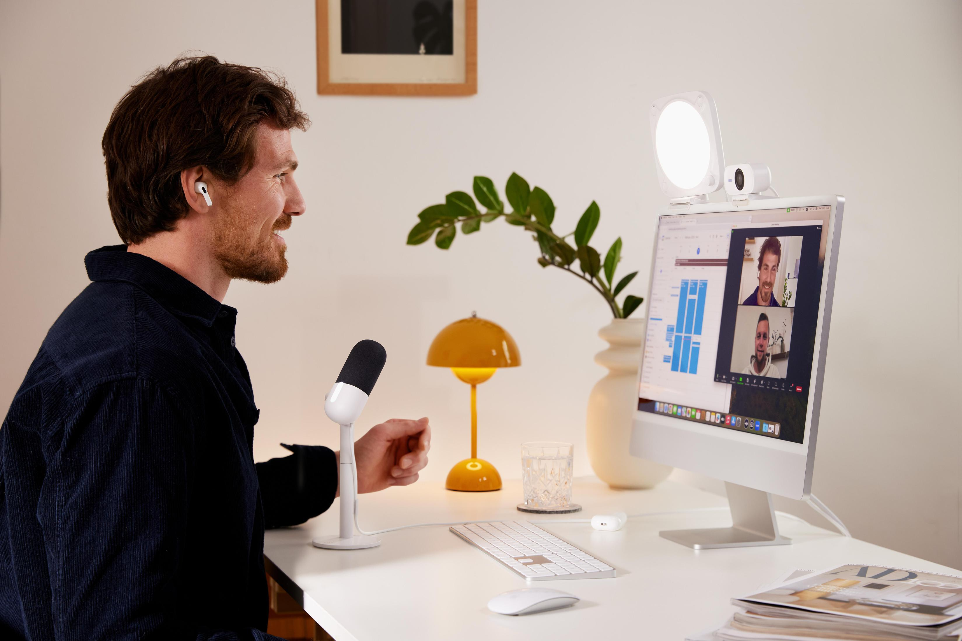 Mann im Videoanruf, mit Mikrofon und Licht. Computer mit Videoanruf auf dem Schreibtisch.