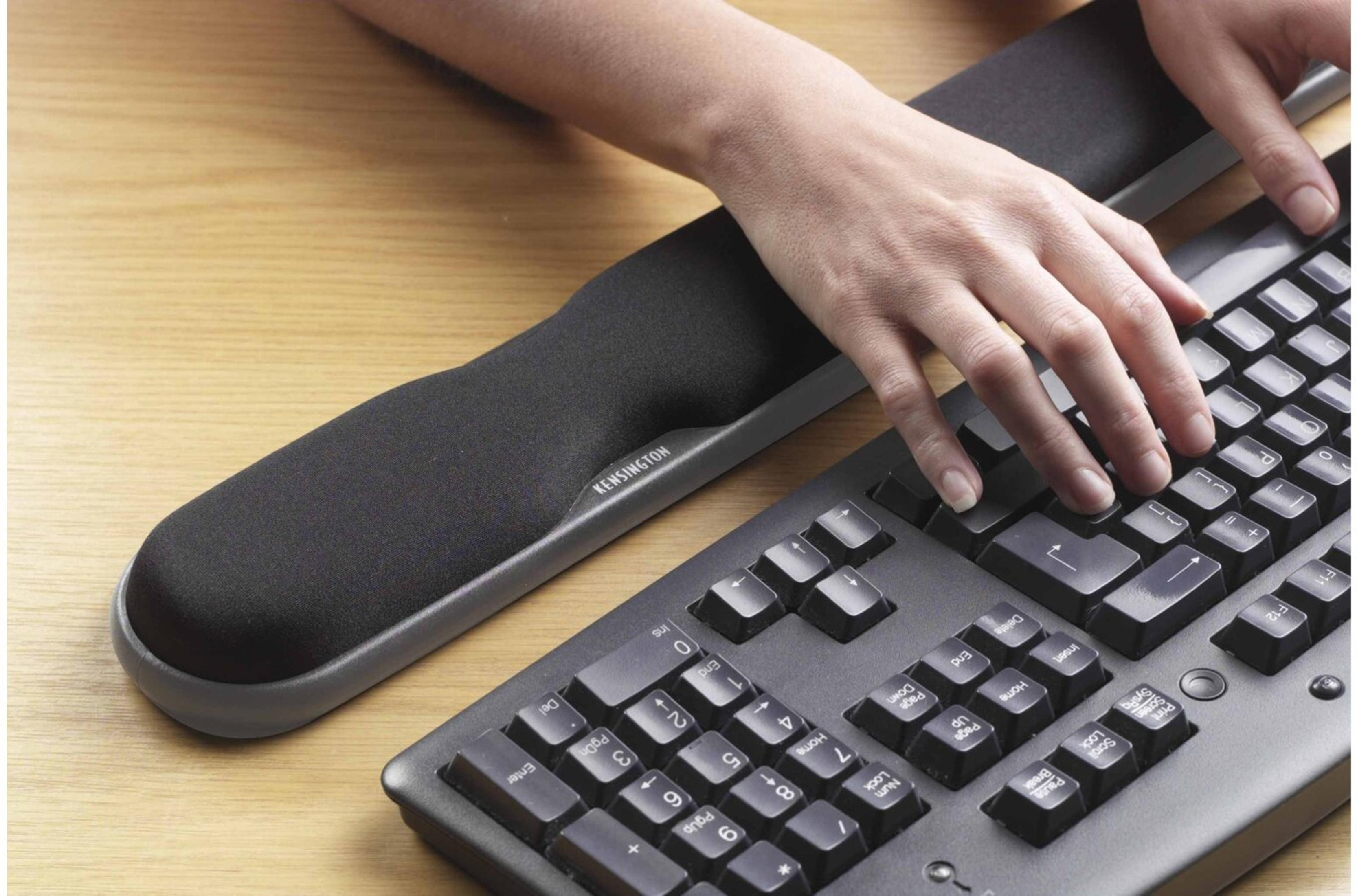 Mano de persona en teclado con reposamuñecas. Teclado y reposamuñecas en escritorio de madera.