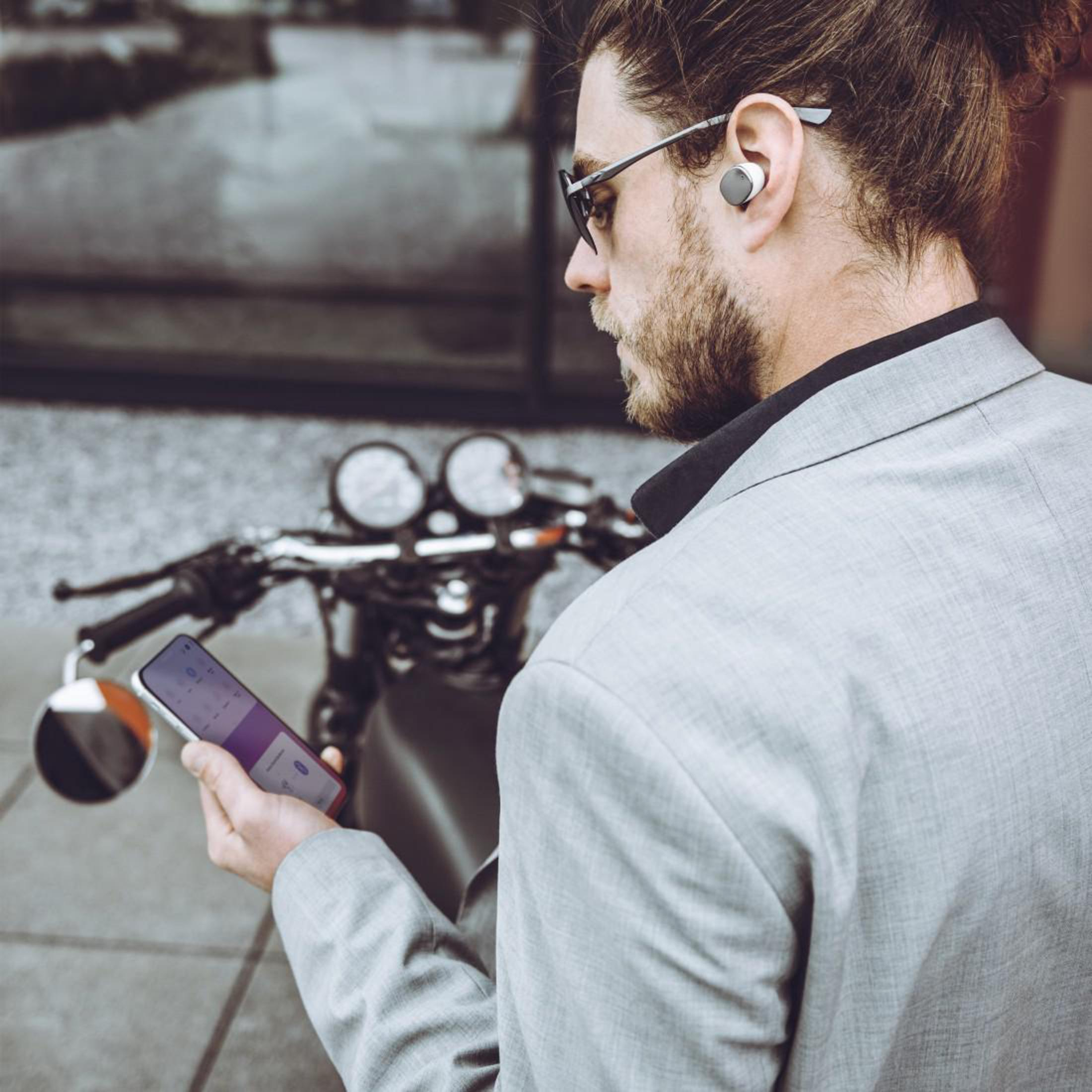 Mann mit Ohrhörern, hält Telefon. Motorrad im Hintergrund. Draußen.