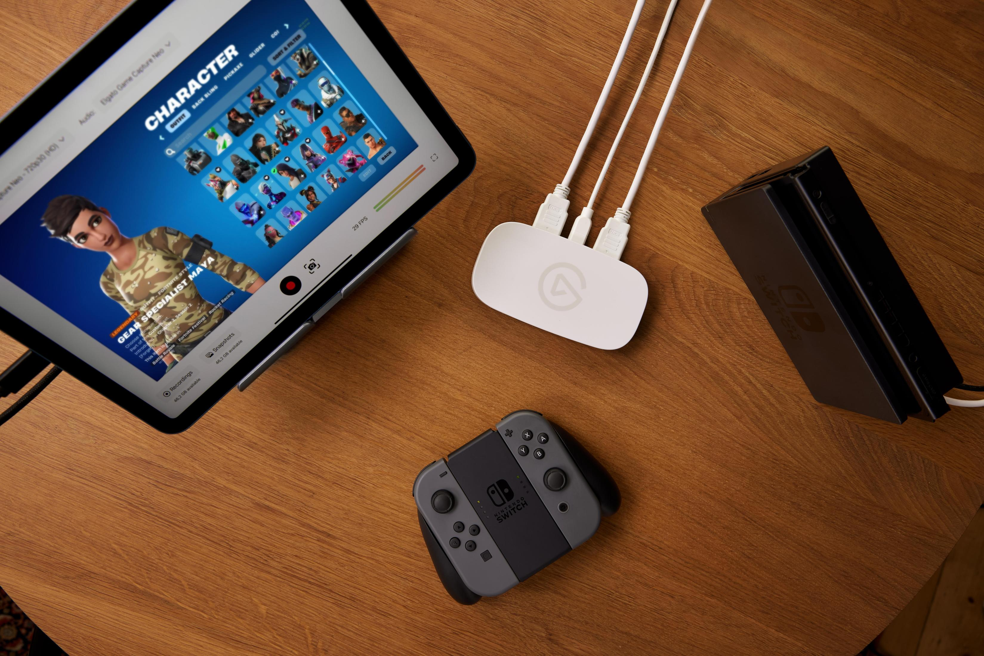 Tableta mostrando selección de personajes de juego junto a dispositivo de captura y consola Switch.