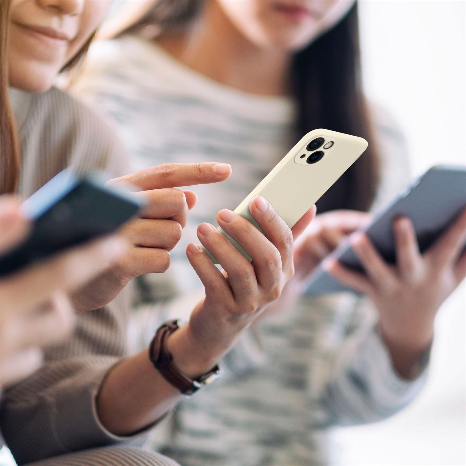 Drei Personen schauen auf Telefone, eine Person hält ein Telefon mit cremefarbener Hülle im Fokus.