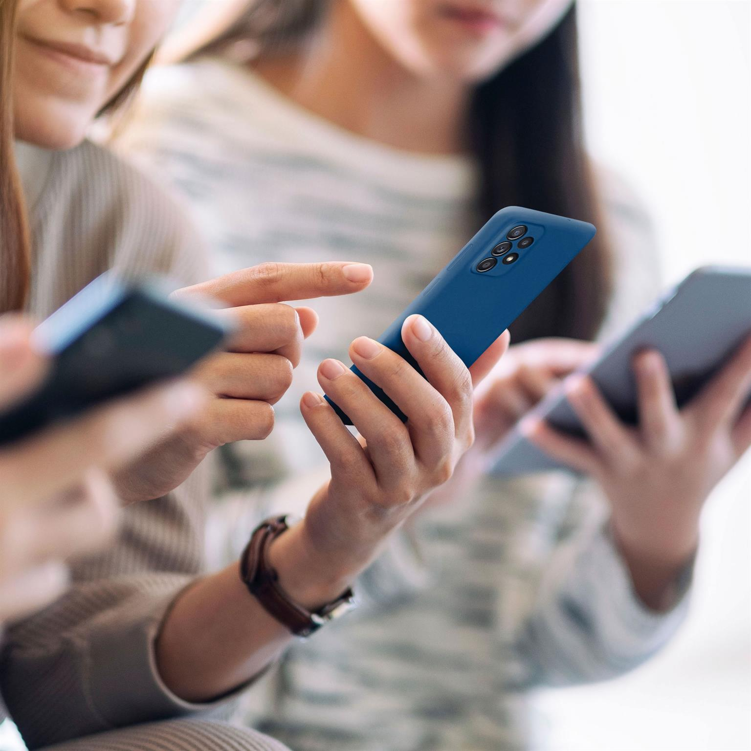 Drei Personen, Hände halten Telefone. Ein Telefon ist blau.
