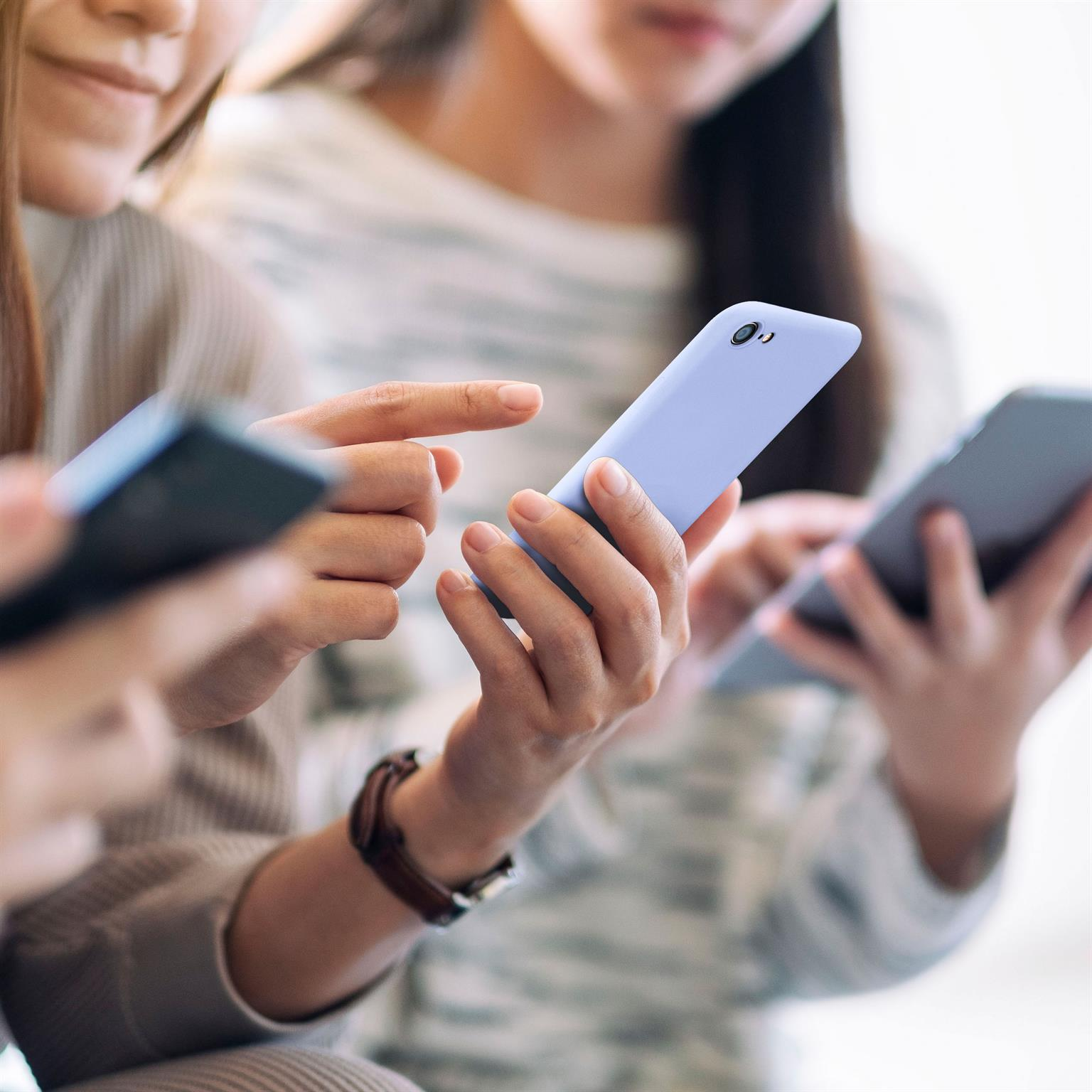 Drei Personen halten Smartphones. Eine Person zeigt auf ein blaues Telefon. Andere Telefone sind grau.