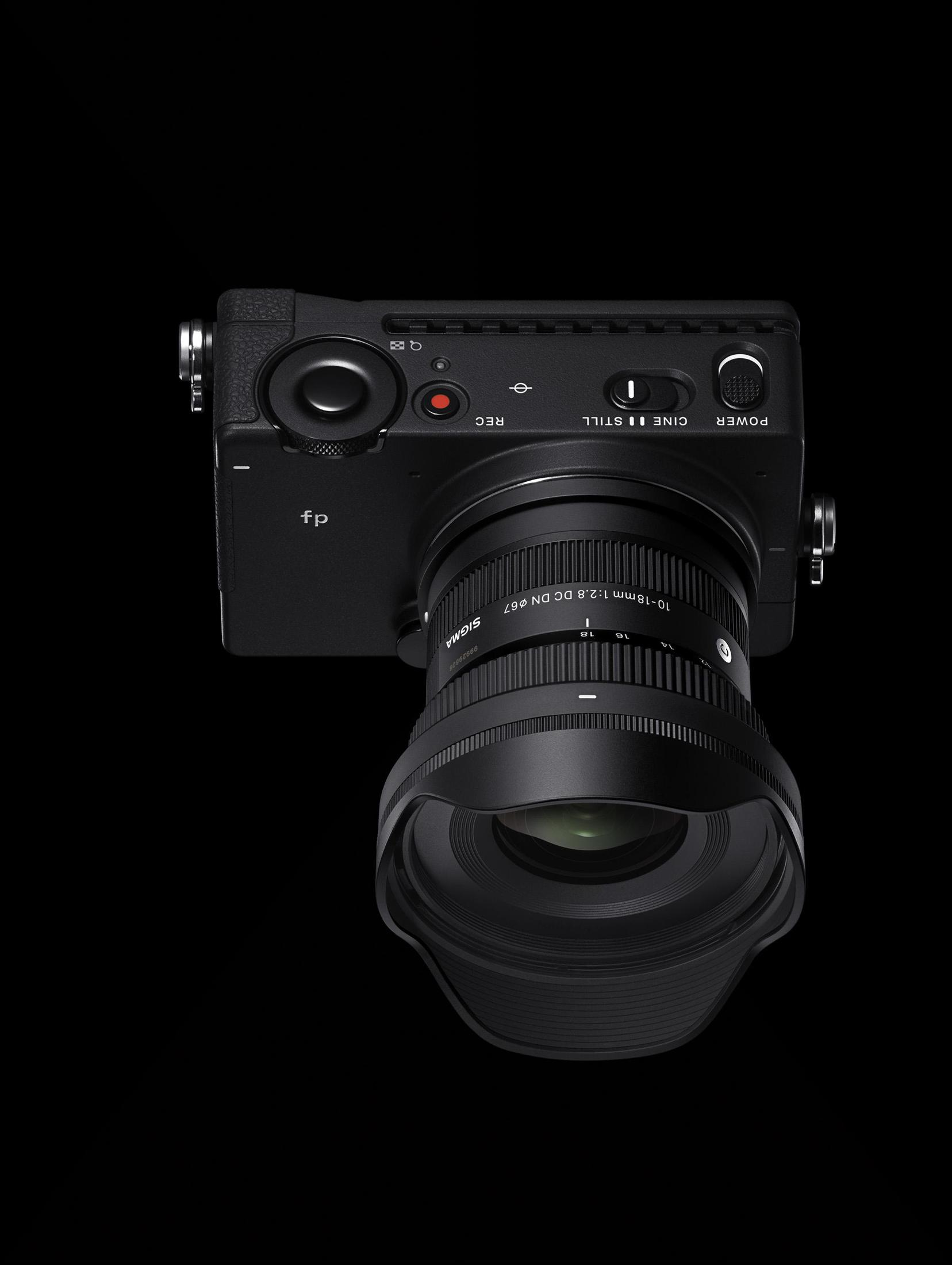 Czarny aparat z obiektywem skierowanym w dół. Czarne tło. Widoczne elementy sterujące i ustawienia.