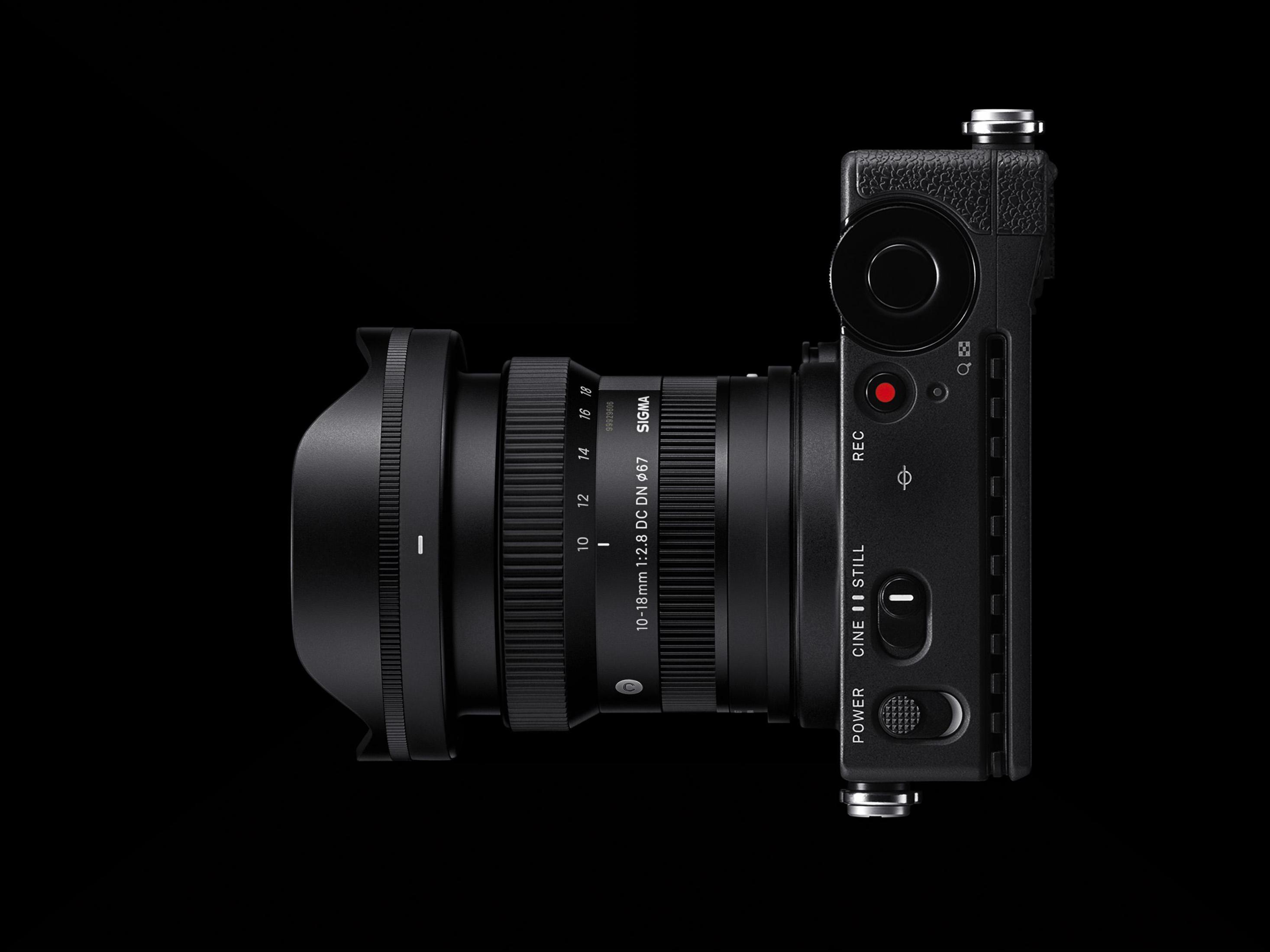 Czarny aparat z obiektywem, widok z boku, na czarnym tle. Widoczne REC i inne przyciski.