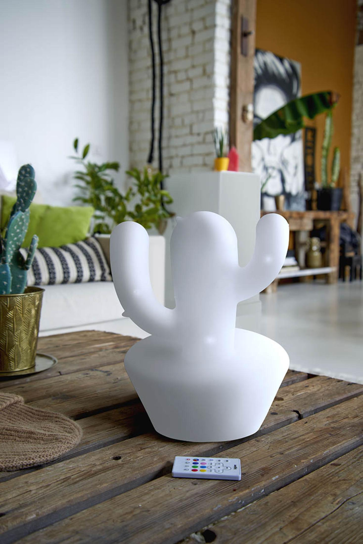 Biała lampa w kształcie kaktusa na drewnianym stole. Pilot z przodu. Sofa w tle.