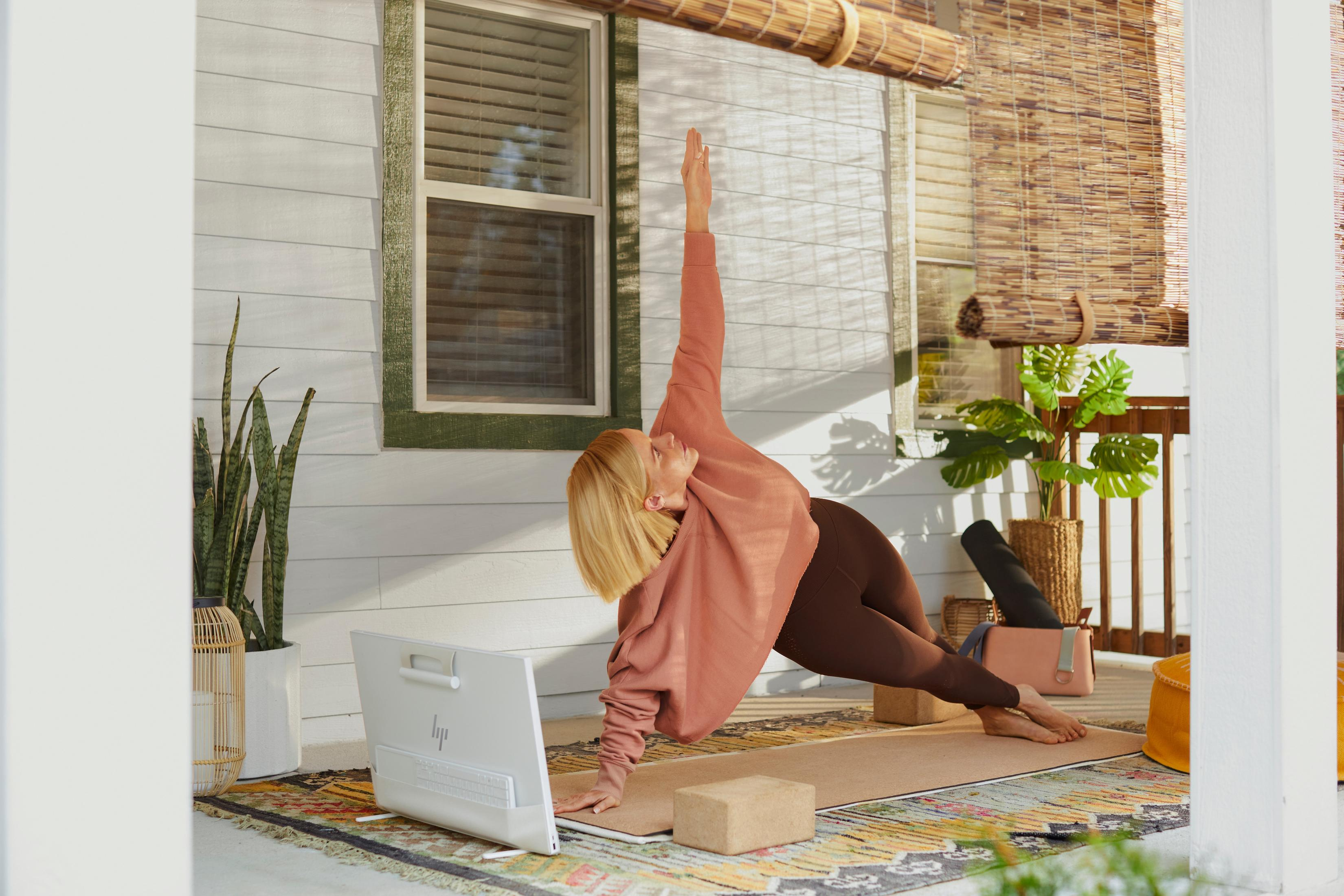 Kobieta uprawia jogę na werandzie, widoczny laptop i sprzęt do jogi.