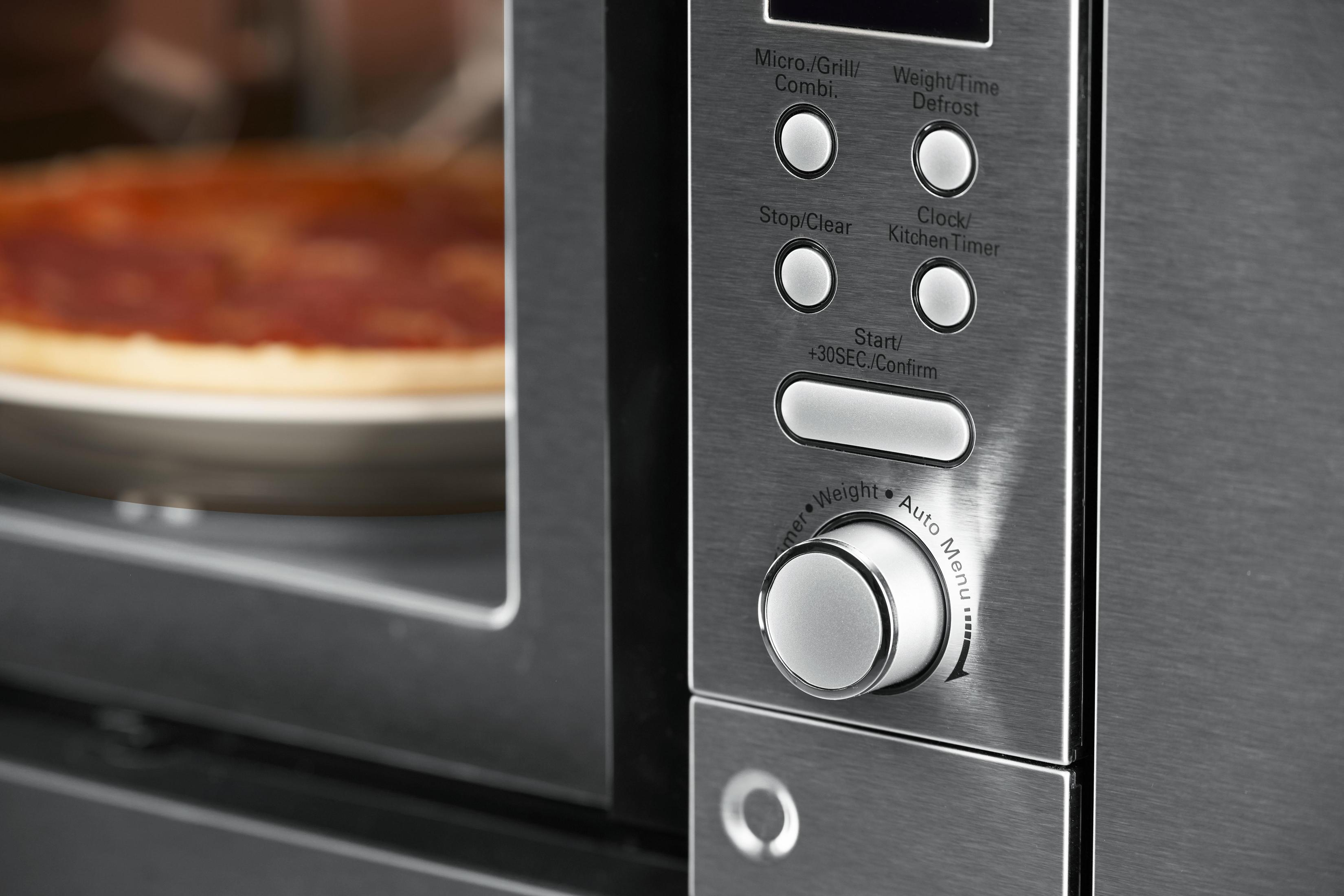 Close-up of a microwave control panel with buttons and a dial, pizza in the background.