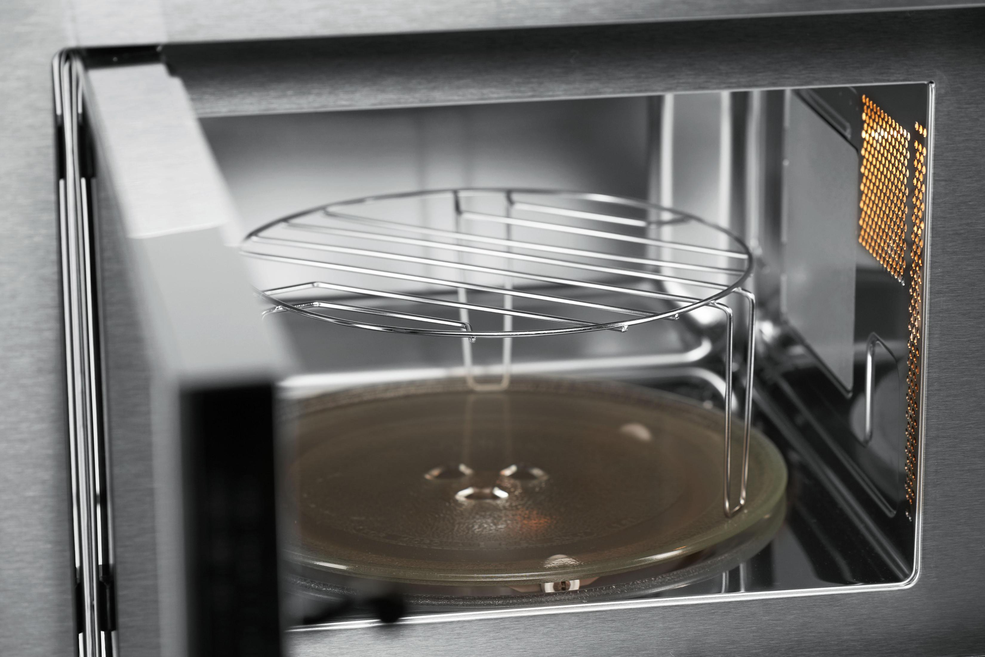 Interior of a microwave with a wire rack and glass plate. Open door. Silver finish.