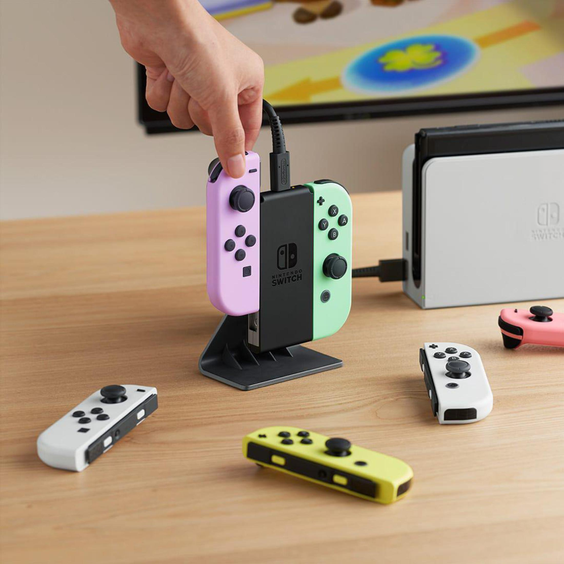 Mano che inserisce un Joy-Con in una stazione di ricarica con altri controller e Switch.