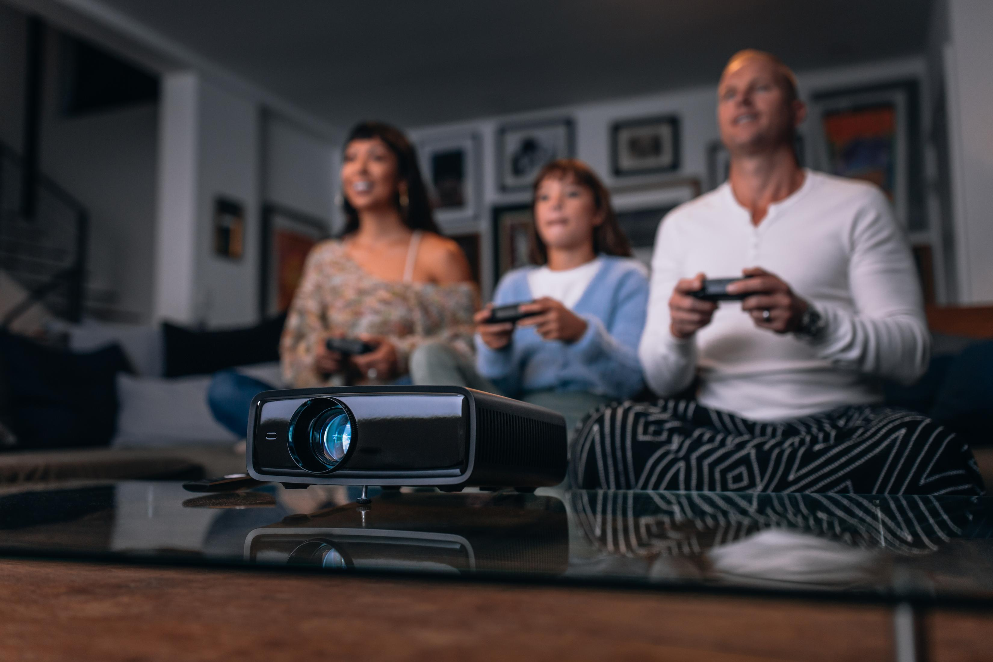 Rodzina gra w gry wideo. Projektor wyświetla grę na ścianie. Salon.