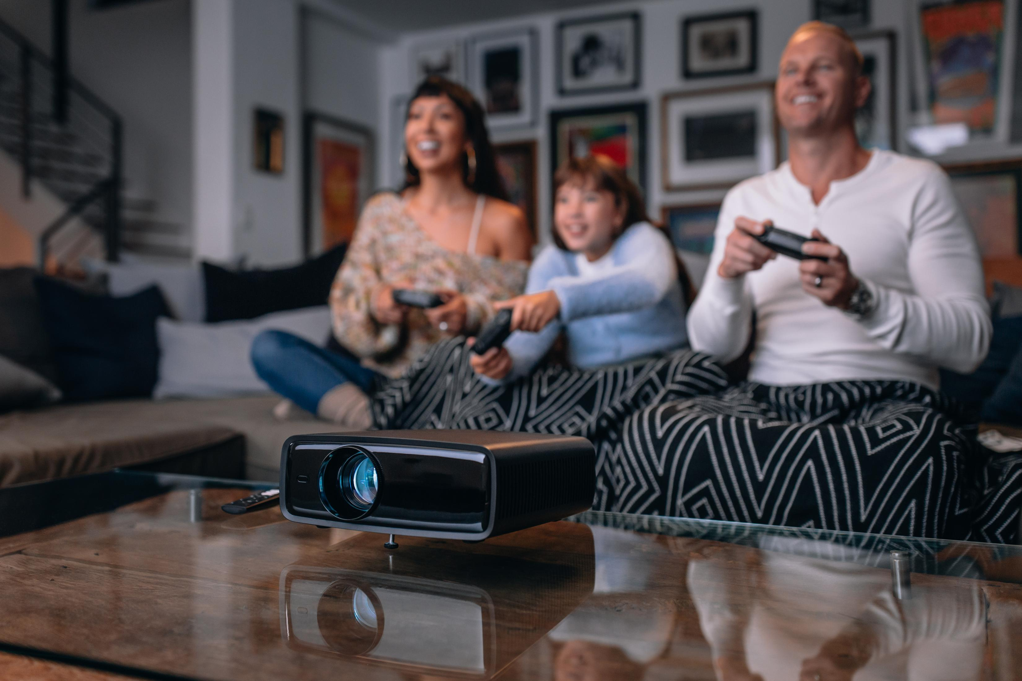 Rodzina gra w gry wideo na kanapie. Projektor wyświetla grę na ścianie. Szczęśliwe miny.