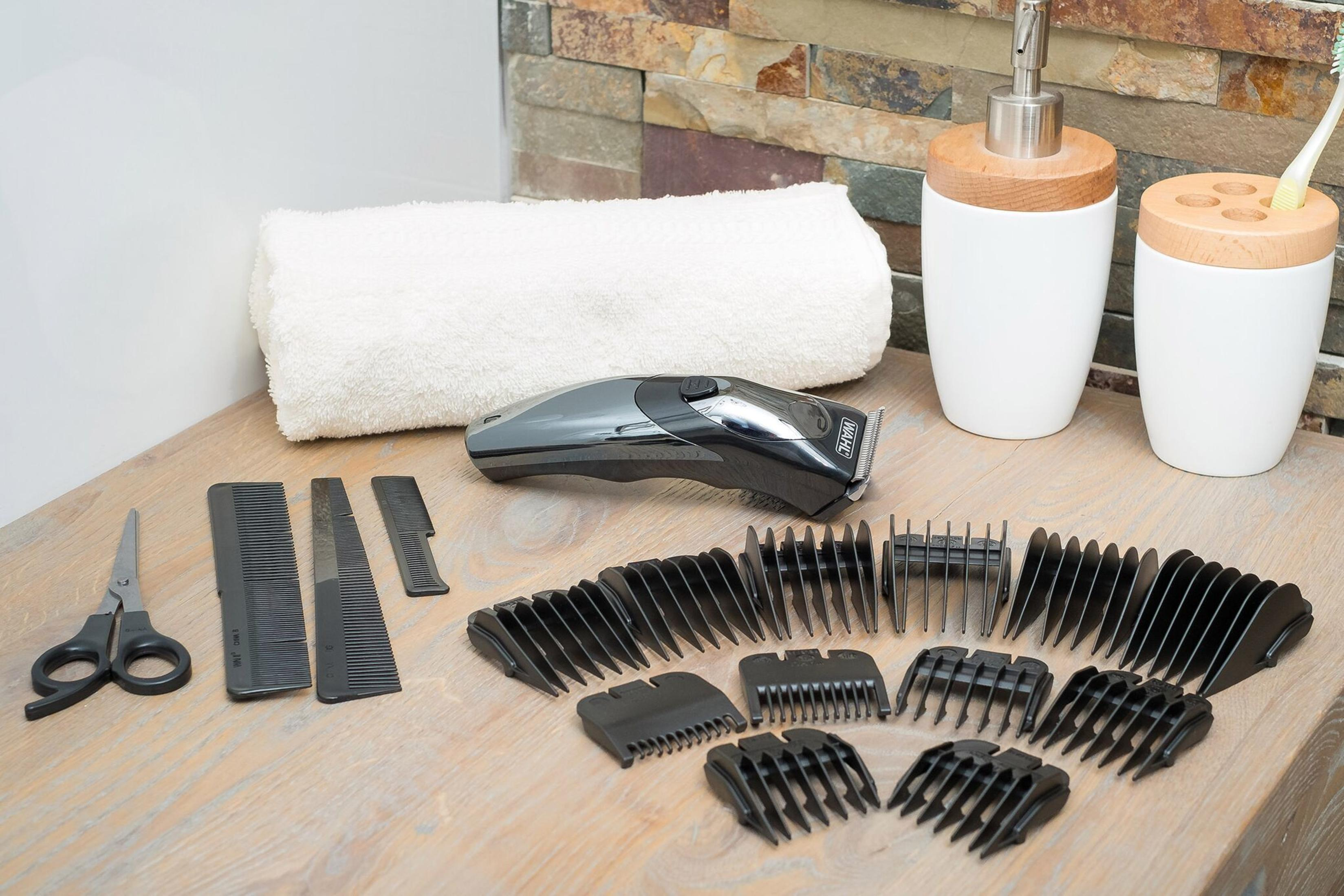 Badezimmer-Theke mit Pflegeutensilien: Clipper, Schere, Kämme und Aufsätze. Ein weißes Handtuch und Seife sind vorhanden.