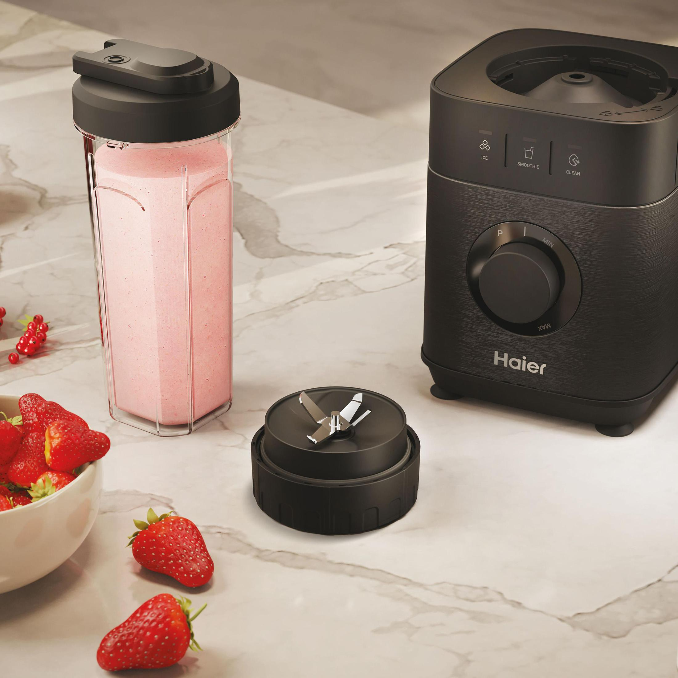 Czarny blender Haier z różowym koktajlem w przezroczystym kubku i truskawkami. Marmurowa powierzchnia.