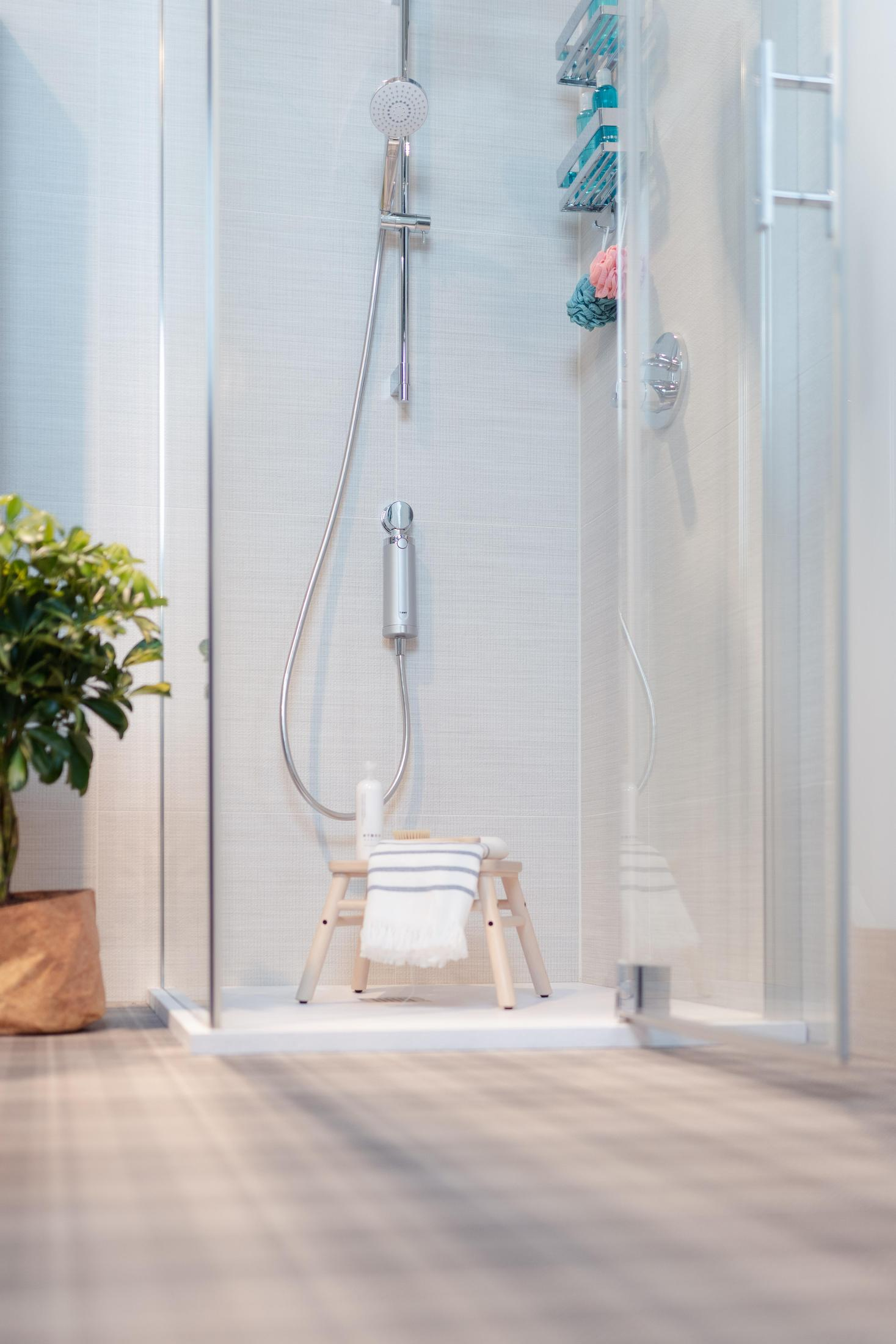 Kabina prysznicowa z prysznicem, stołkiem i kosmetykami. Roślina po lewej stronie szkła.