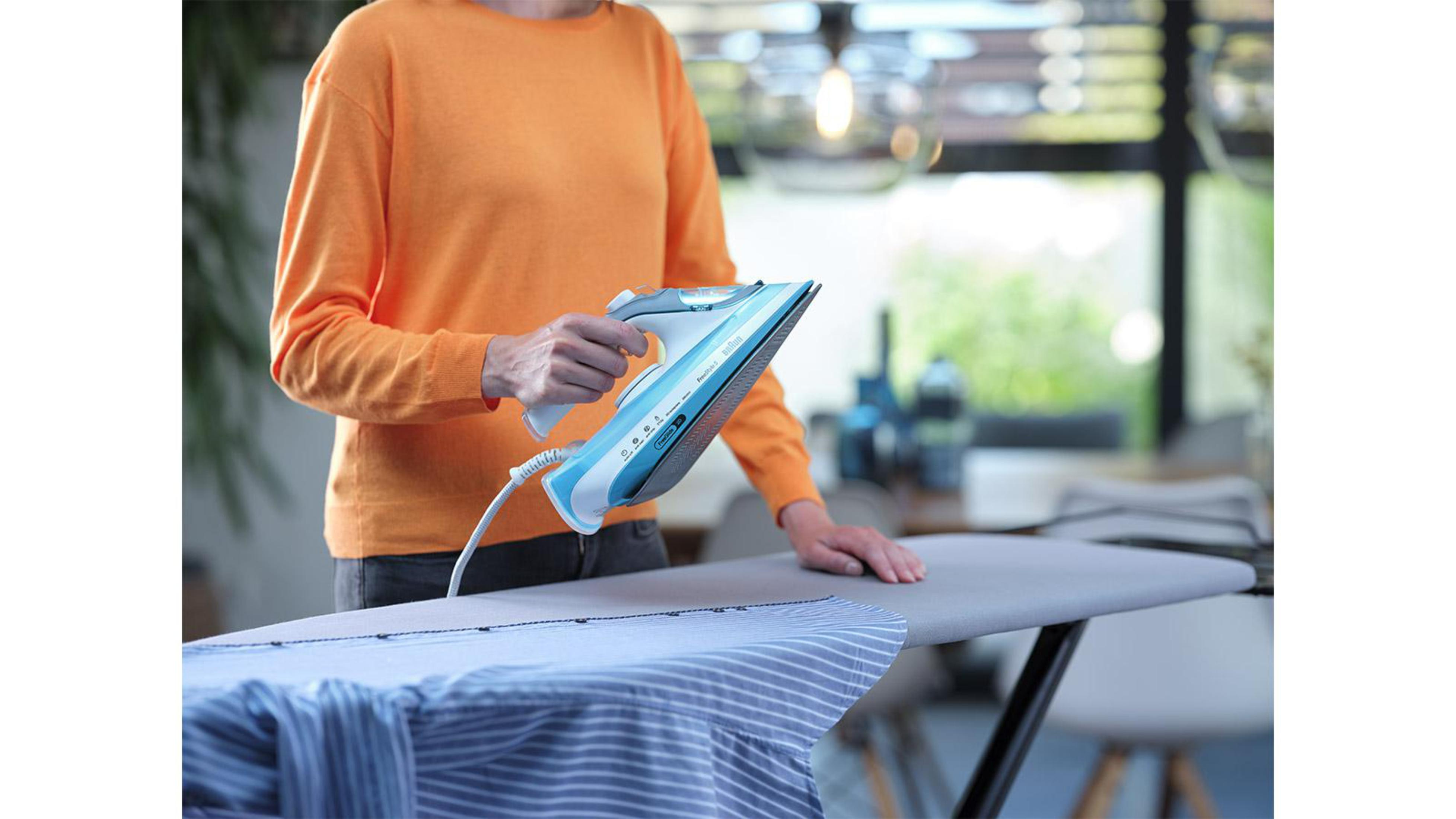 Une femme repassant une chemise rayée sur une planche à repasser avec un fer bleu et blanc.