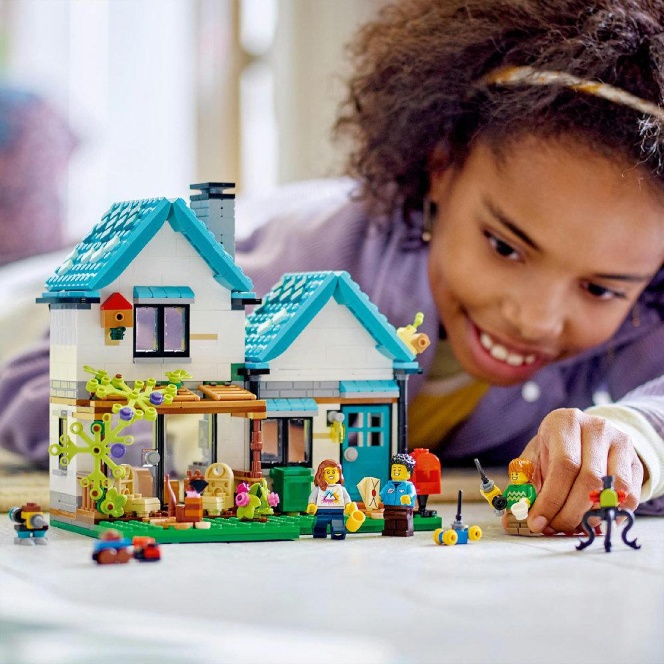 Una ragazza gioca con una casa Lego. È blu e bianca, con personaggi e accessori Lego intorno.