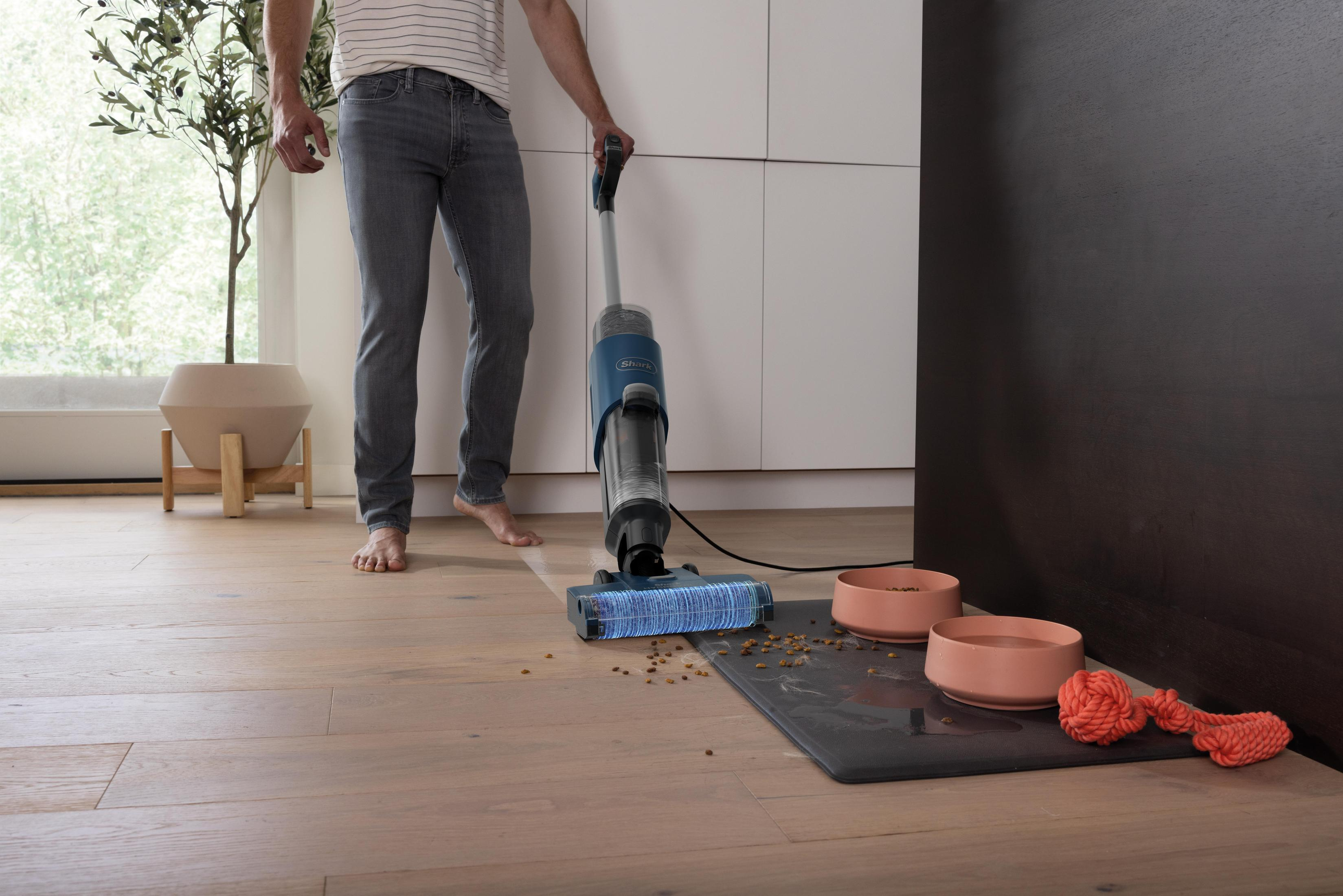 Une personne passe l'aspirateur sur un parquet, avec de la nourriture et des jouets pour animaux à proximité.