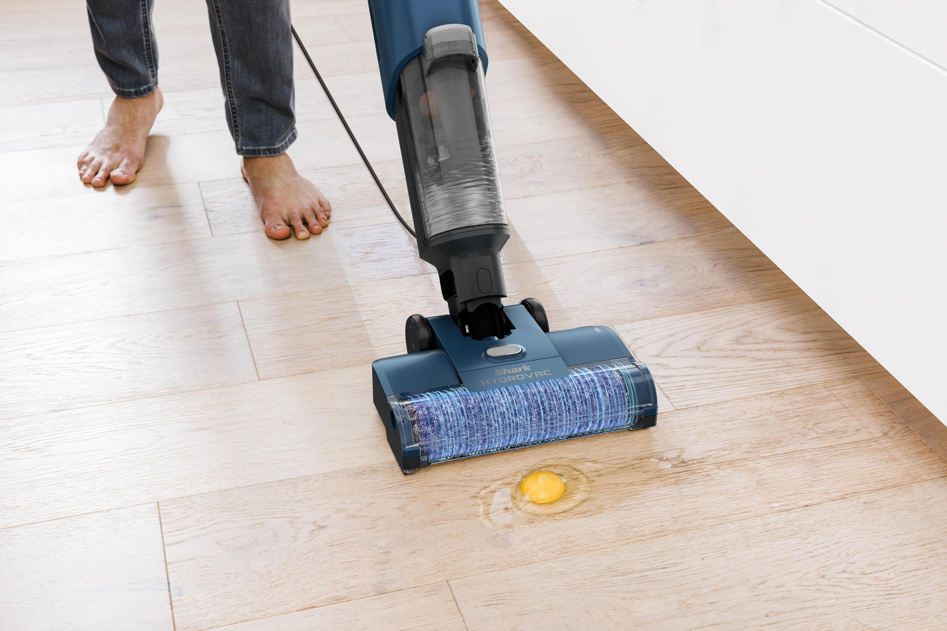 Une personne qui passe l'aspirateur sur un sol avec un aspirateur. Un œuf est cassé par terre.
