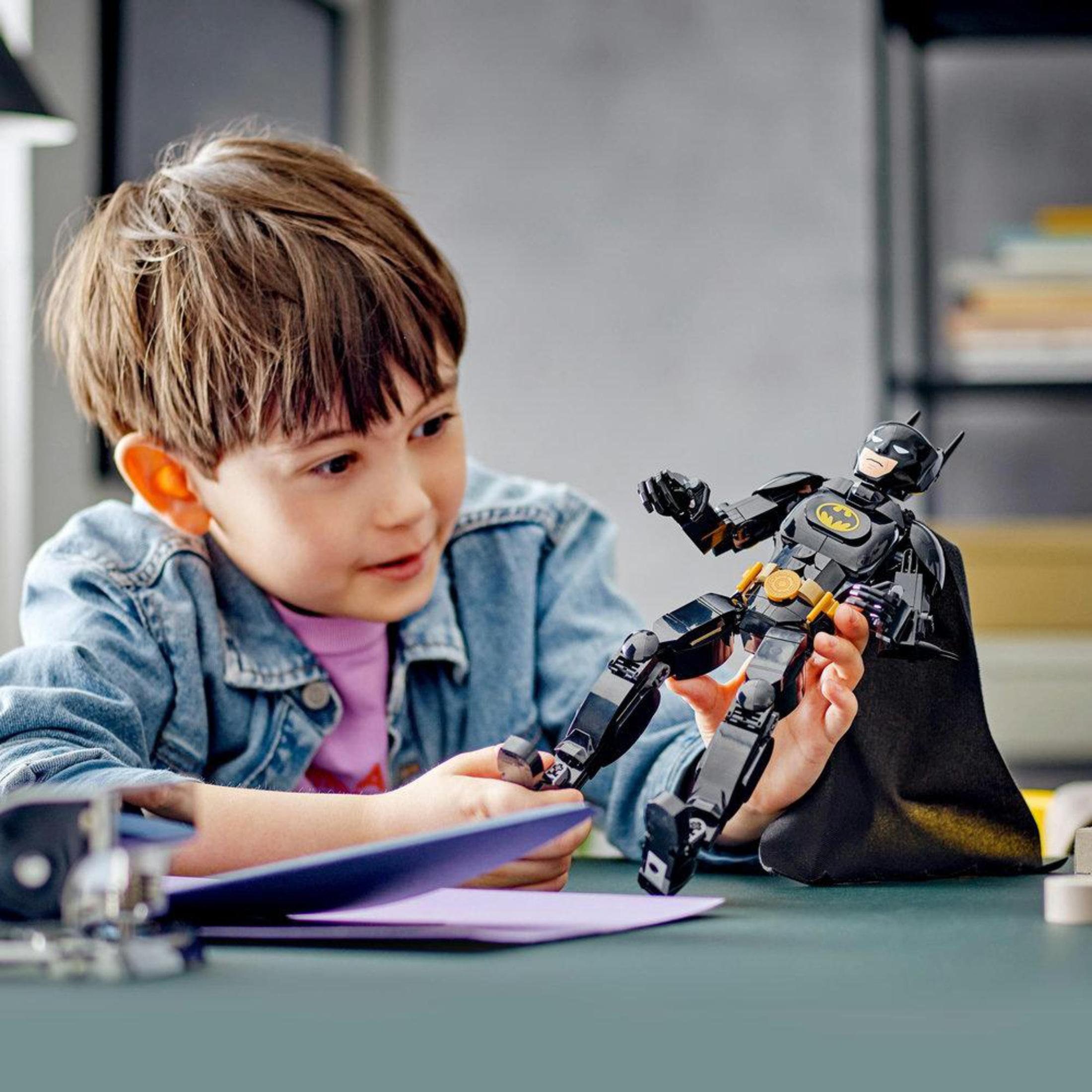 Un niño jugando con una figura LEGO de Batman. El niño está mirando la figura con interés.