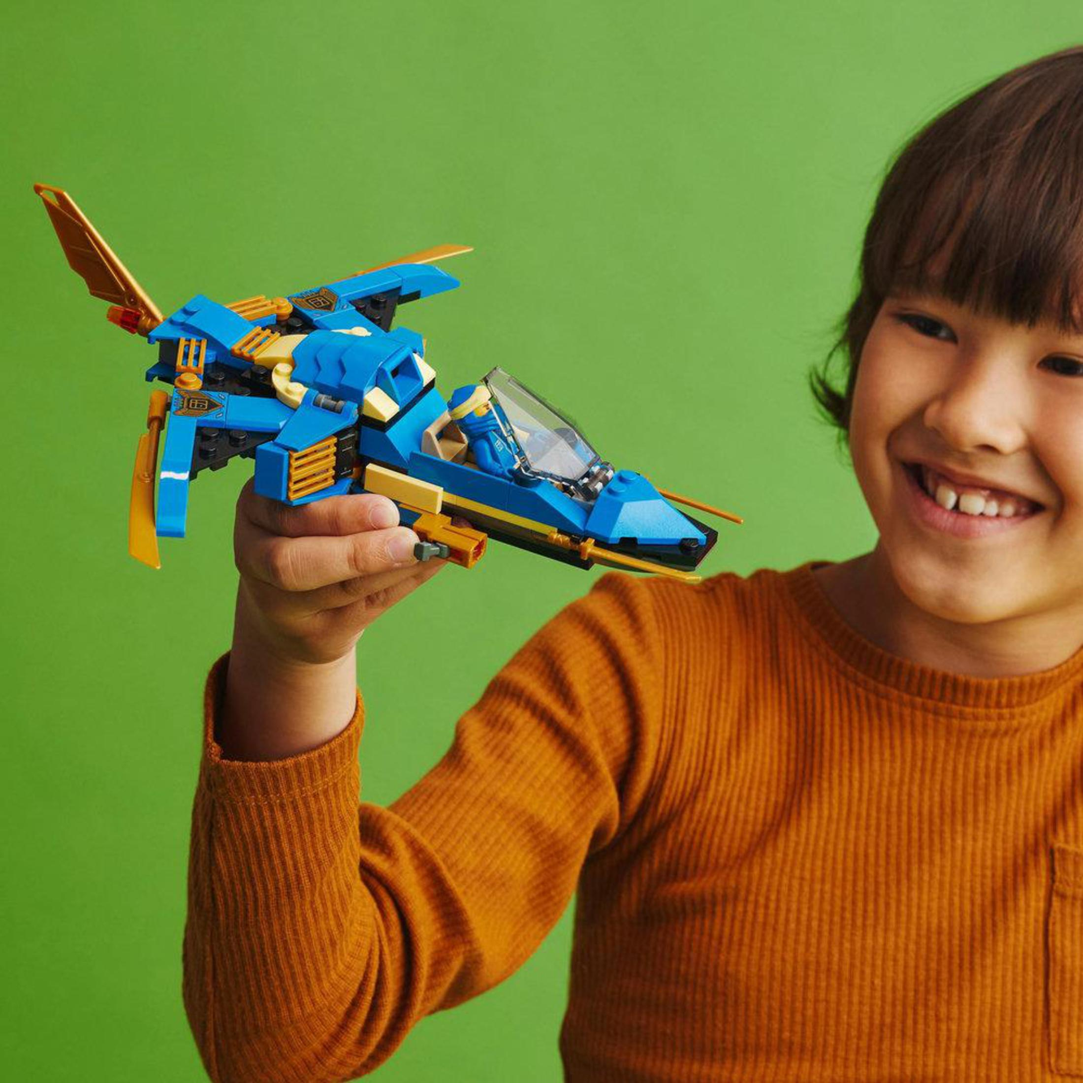 Ein Junge hält ein blaues und goldenes Lego Ninjago-Jet. Er lächelt.