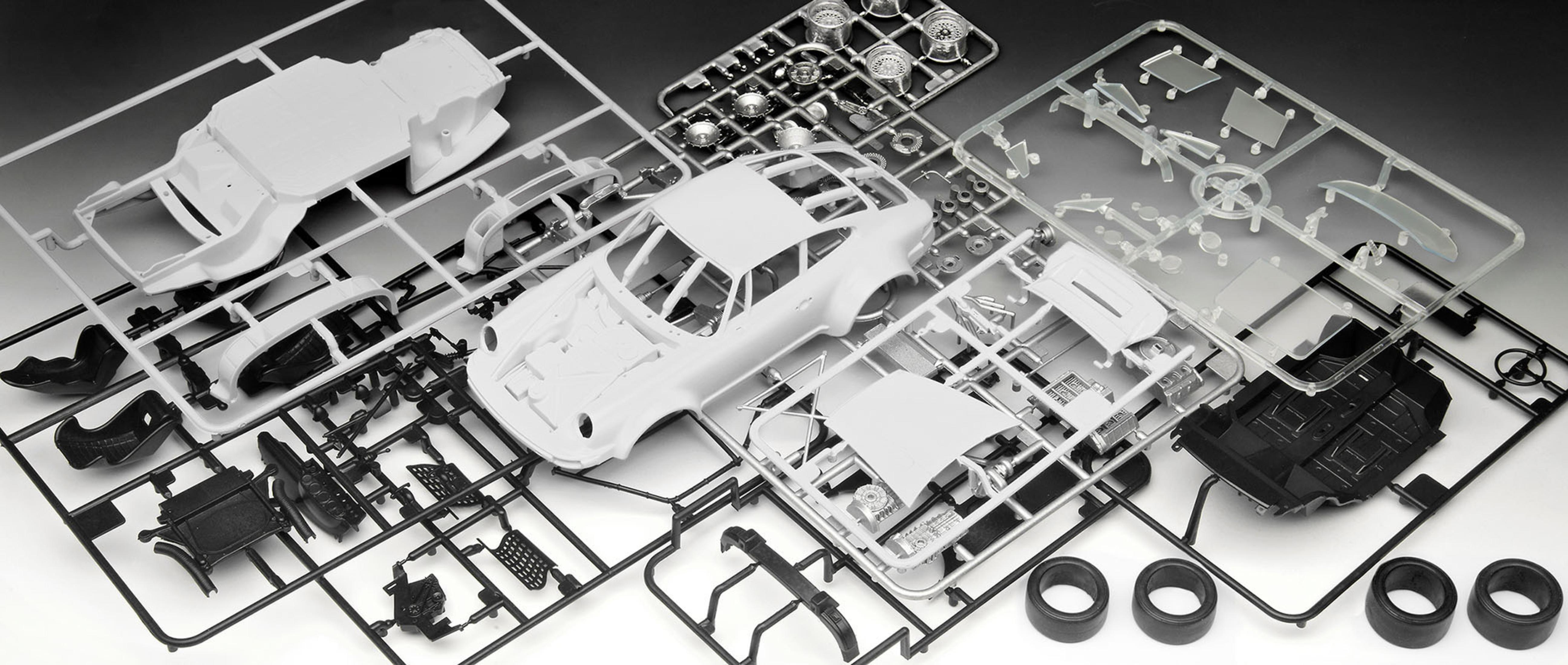 Modelauto-onderdelen, waaronder carrosserie, chassis, wielen en diverse kleine componenten in zwart-wit.