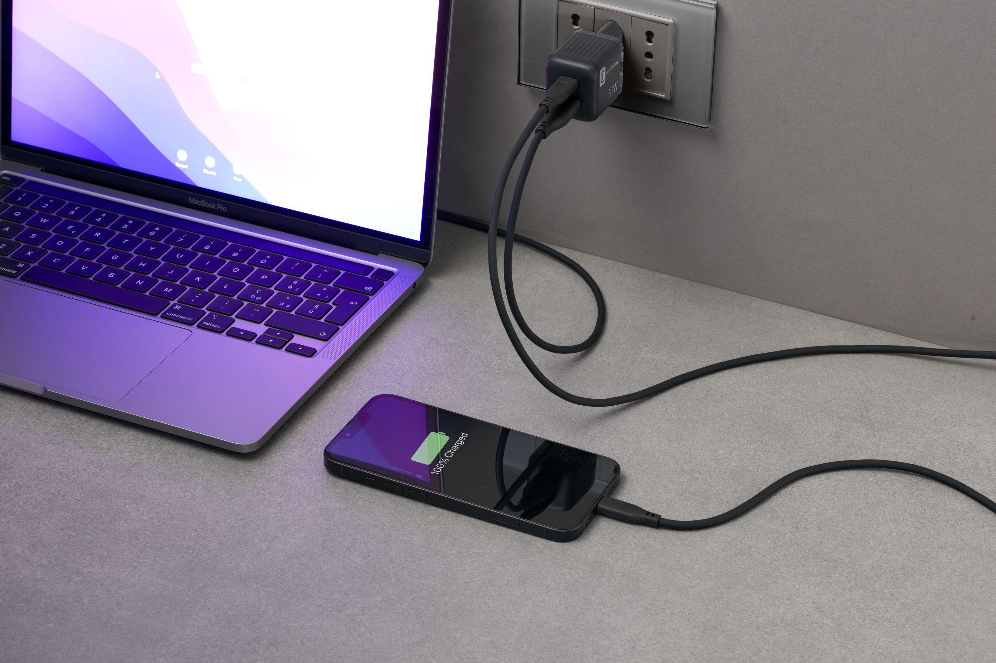 Un laptop e un telefono in carica su una scrivania. Il telefono è in carica, collegato a un adattatore.