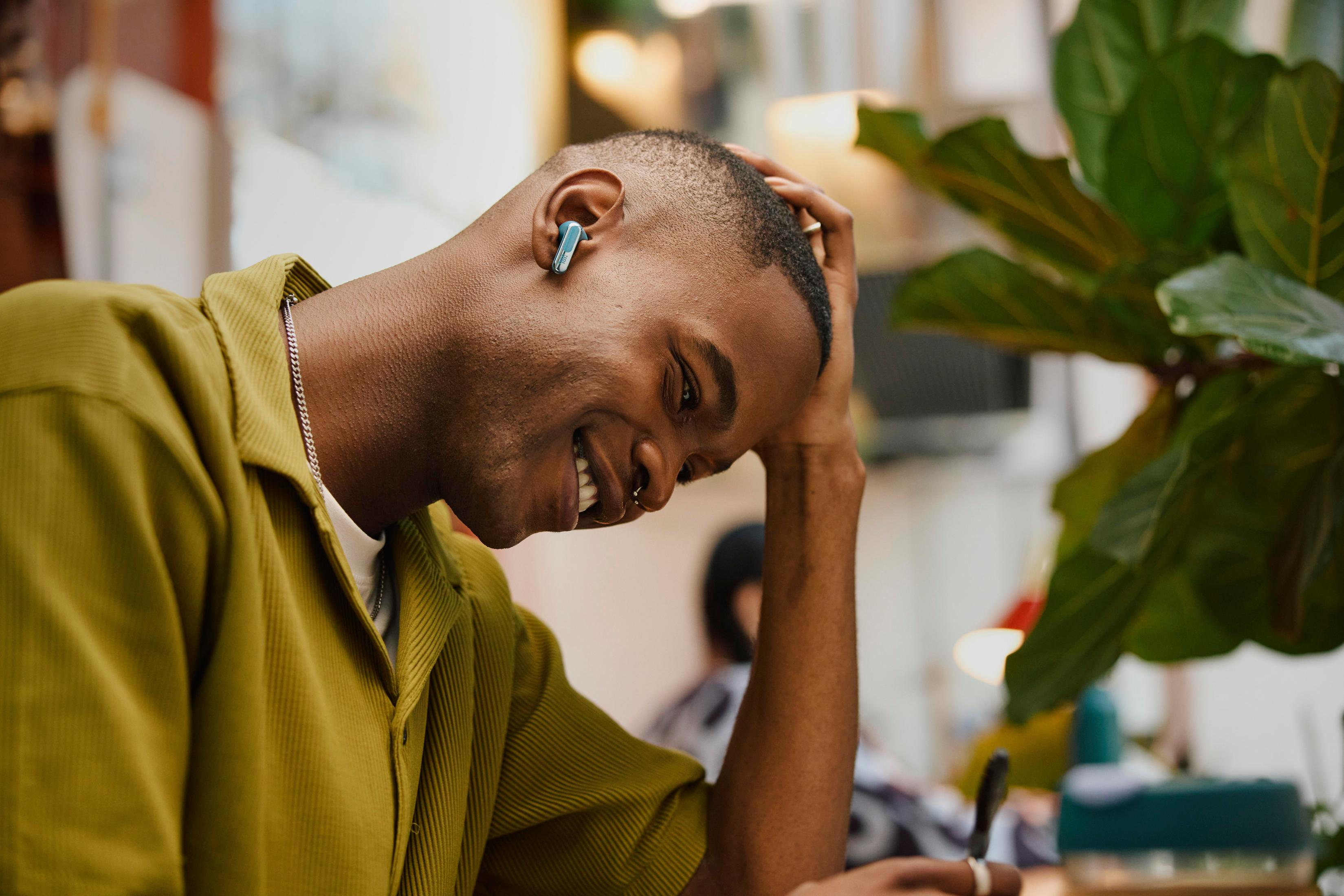 Młody mężczyzna uśmiechnięty, piszący. Ma na sobie żółtą koszulę, słuchawkę w lewym uchu.