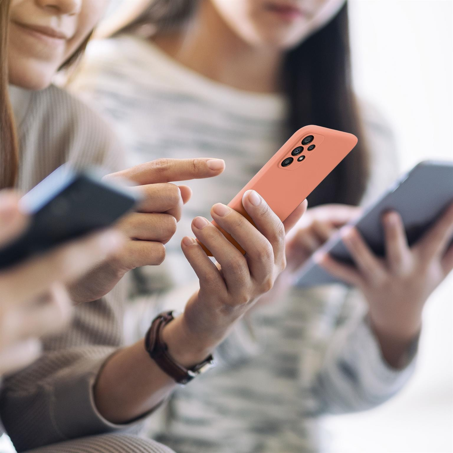 Zwei Frauen halten Telefone mit einer korallenfarbenen Handyhülle, Fokus auf Hülle und Hände.