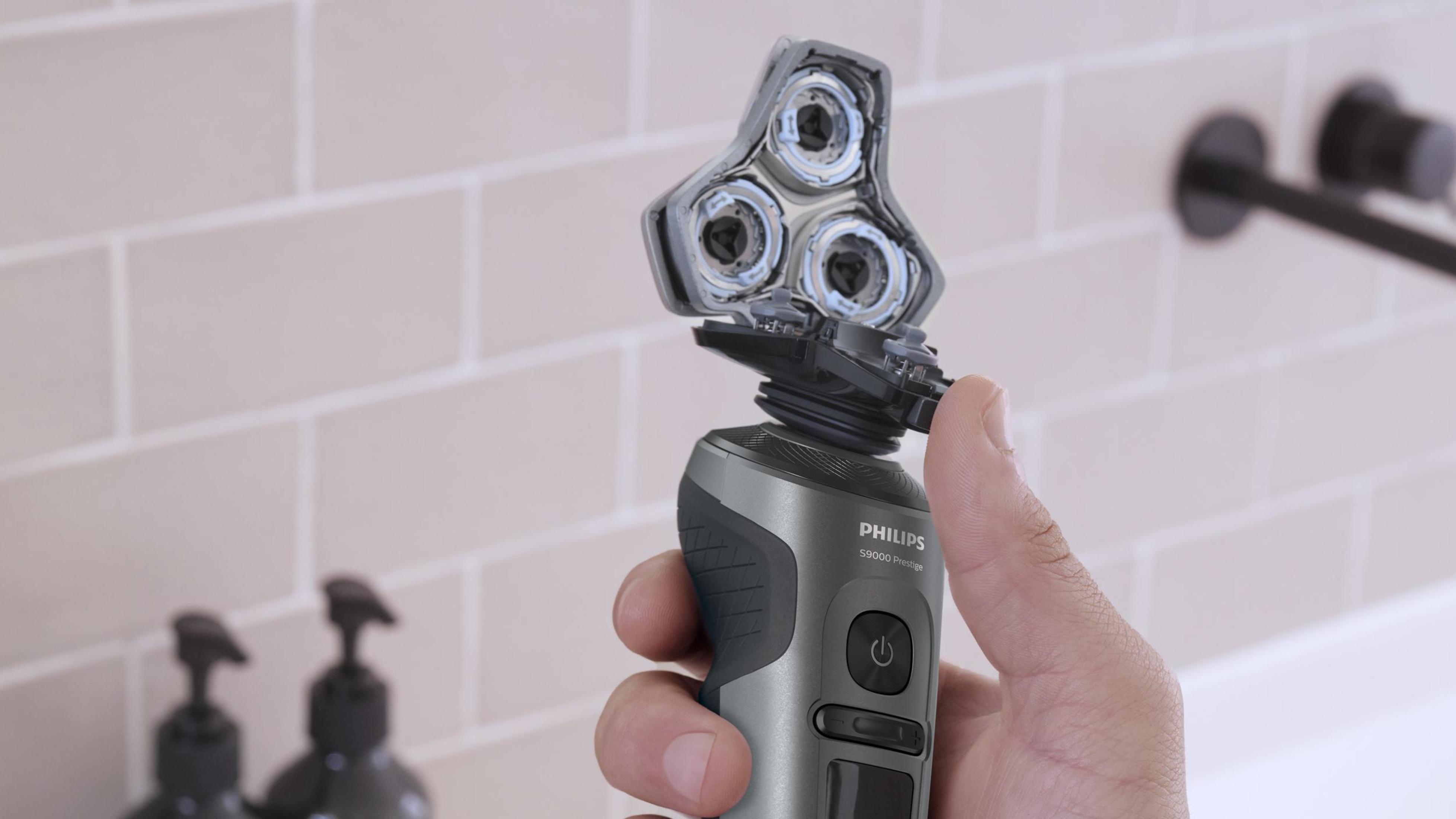 Bir adamın eli Philips elektrikli tıraş makinesini tutuyor, tıraş başlıkları açık, banyo ortamında.