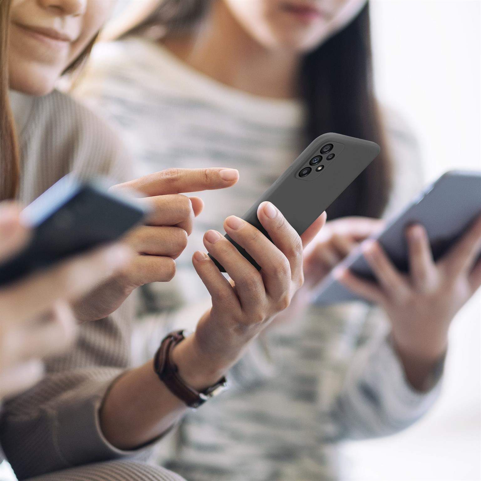 Drei Personen benutzen Smartphones. Eine Hand hält eine dunkelgraue Handyhülle.