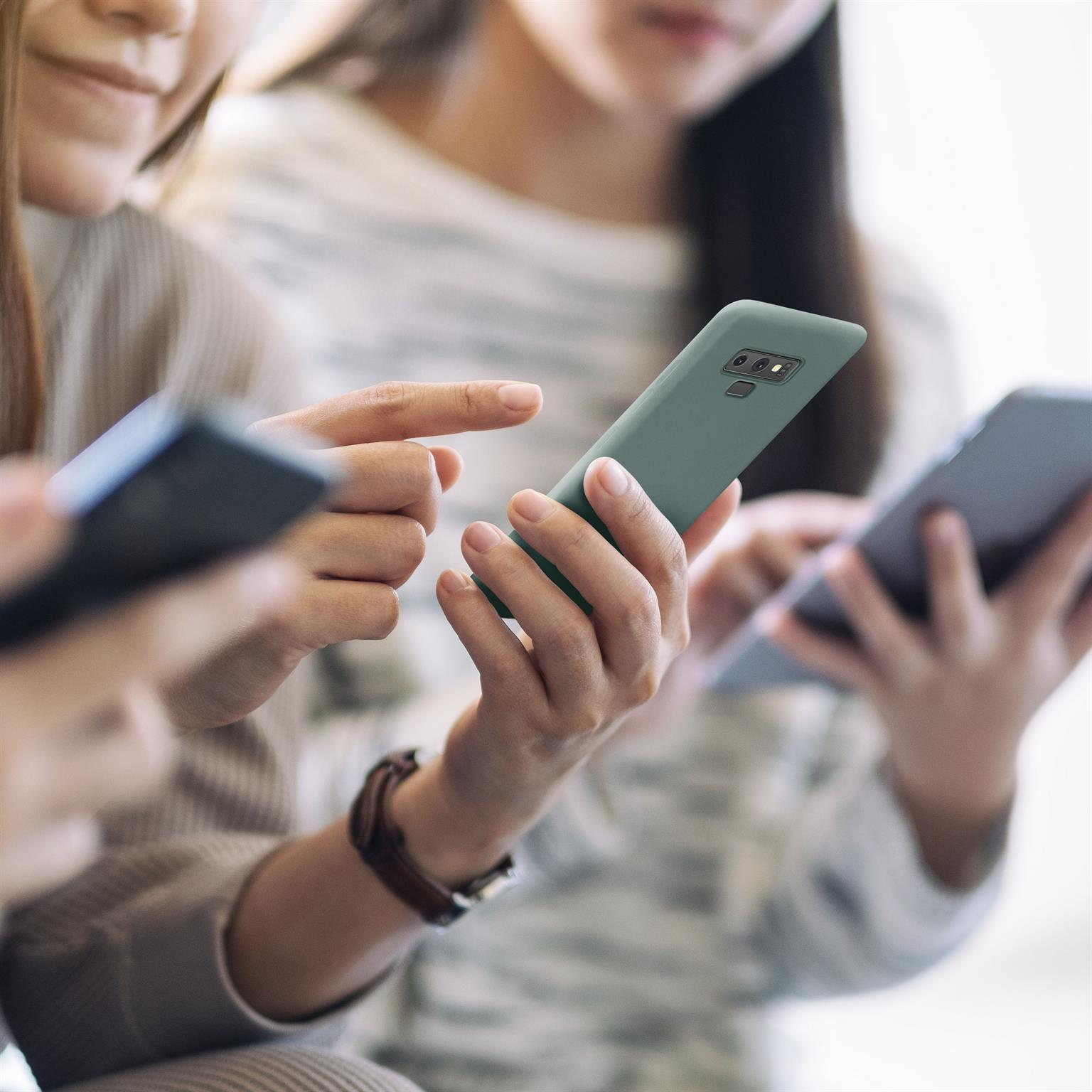 Drei Personen halten Telefone. Eine Person zeigt auf eine grüne Handyhülle, andere halten Telefone.
