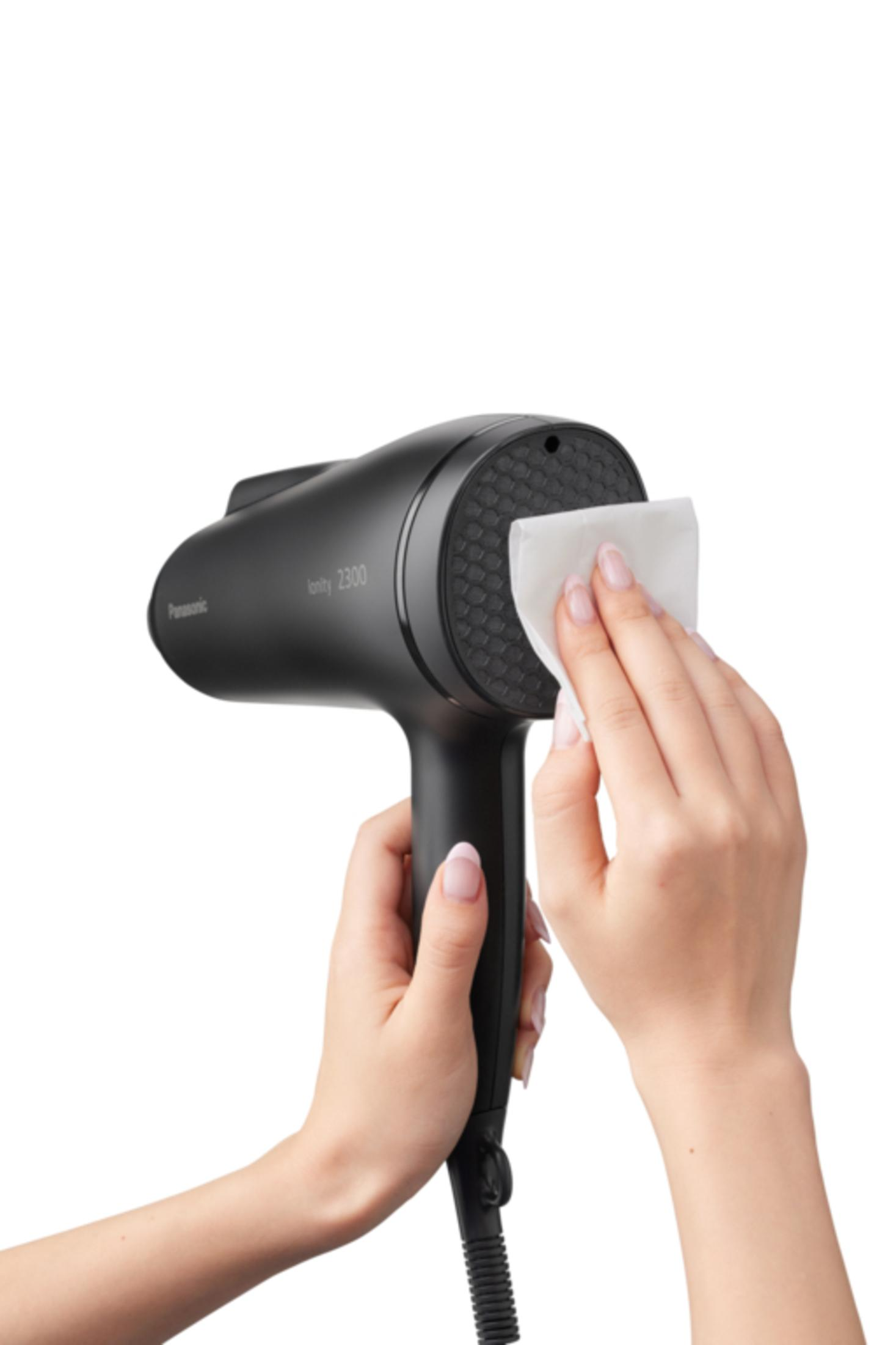 Ręce trzymające czarną suszarkę do włosów z białym papierem, czyszczące powierzchnię.