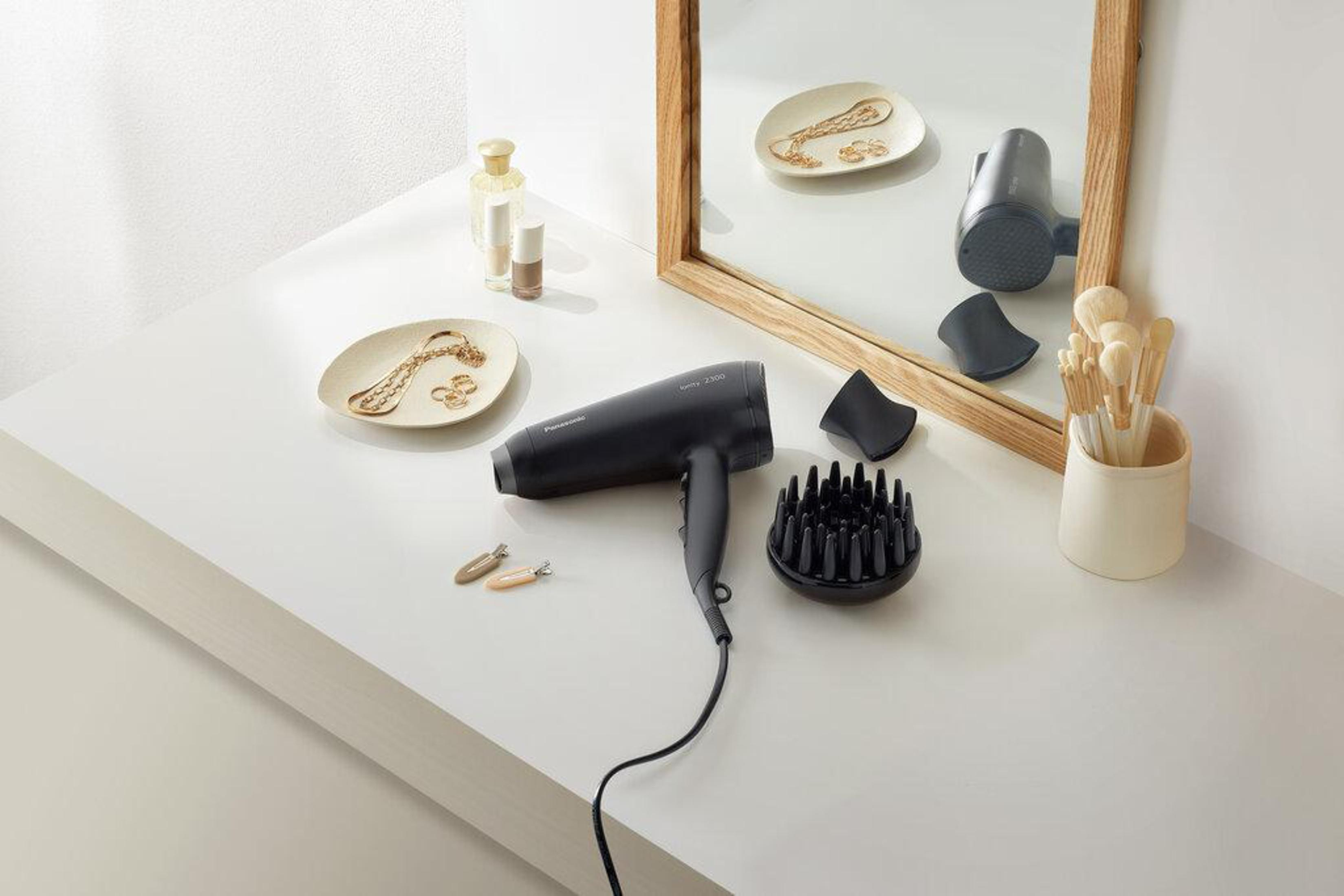 Czarna suszarka na białym stole. Widoczne akcesoria i lustro.